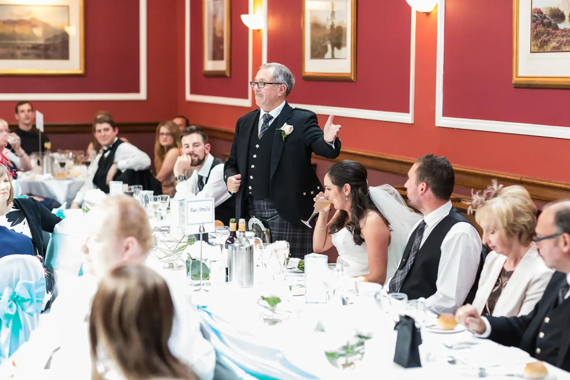 A man in a suit speaking to a group of people at a wedding reception.
