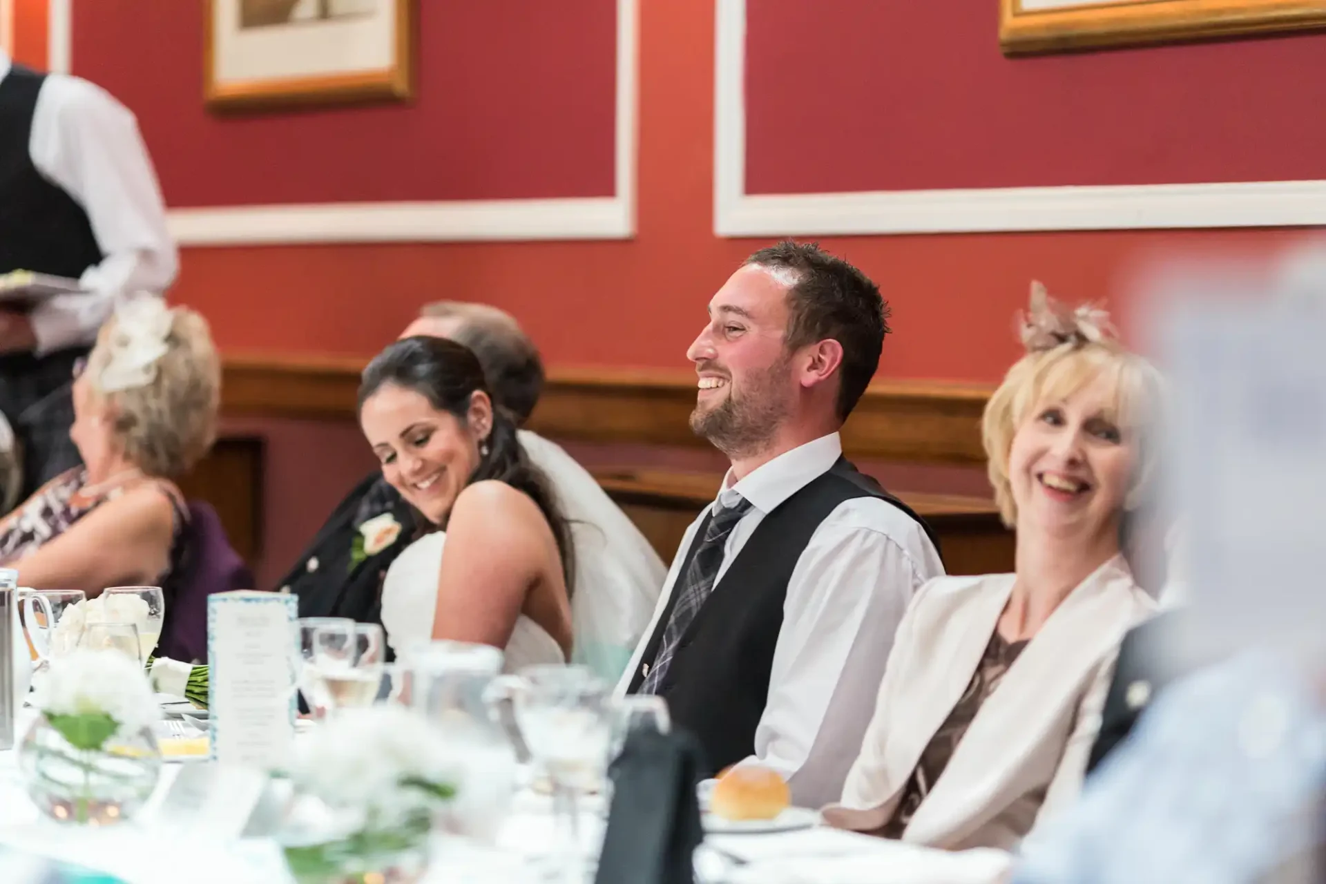 A group of guests at a formal event, smiling and enjoying a conversation at a dinner table.