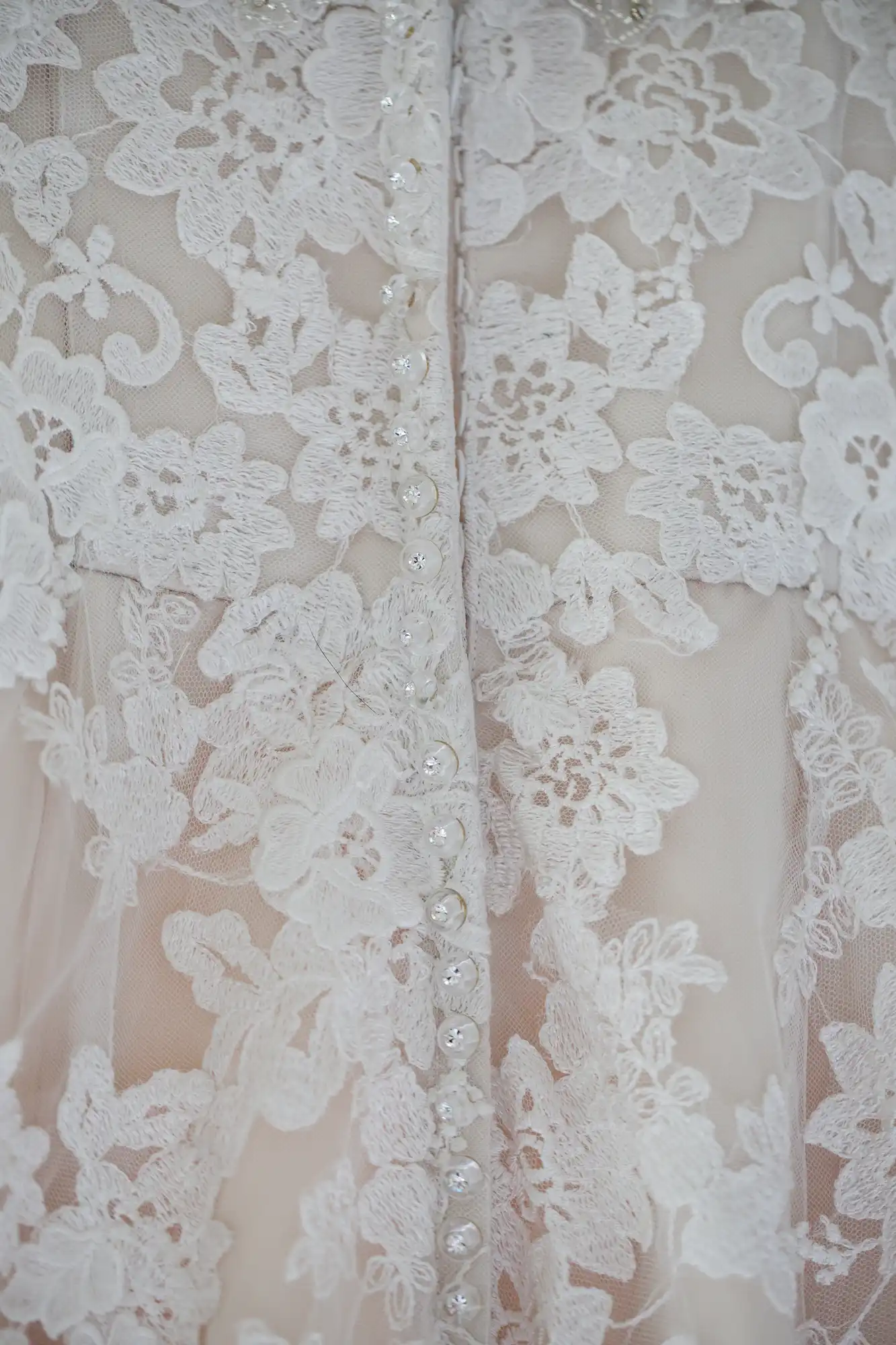 Close-up of a white lace wedding dress featuring a detailed floral pattern and a row of small buttons down the back.