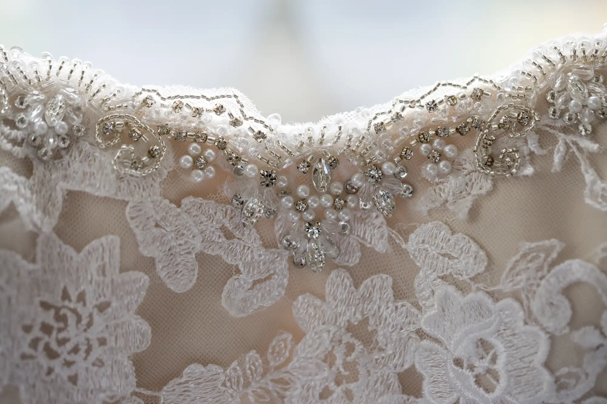 Close-up of a white lace fabric with intricate beadwork and sequin embellishments on the edge.