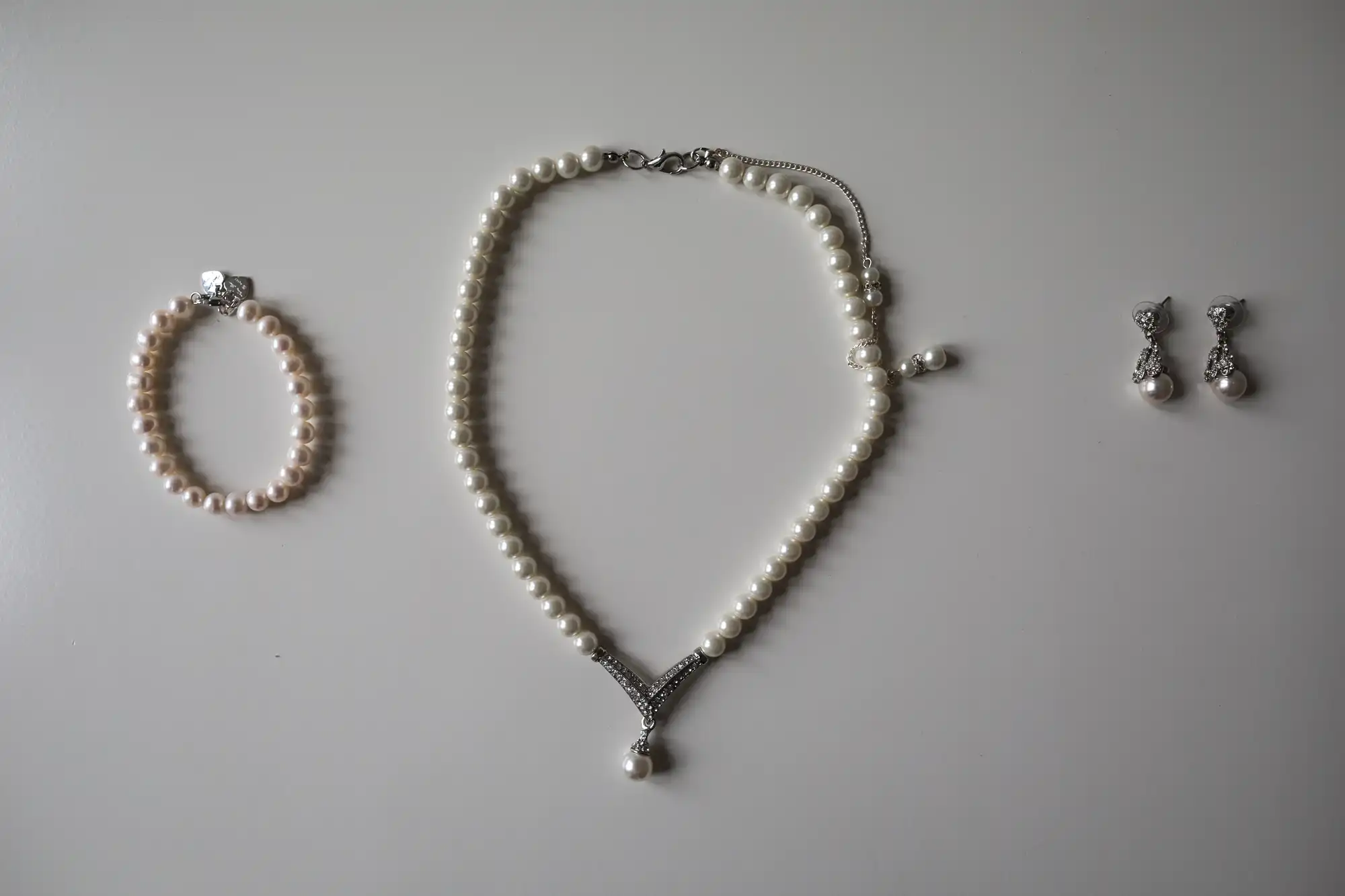 Pearl jewelry set on a white background, including a pearl necklace with a pendant, matching pearl bracelet, and dangle pearl earrings with silver accents.