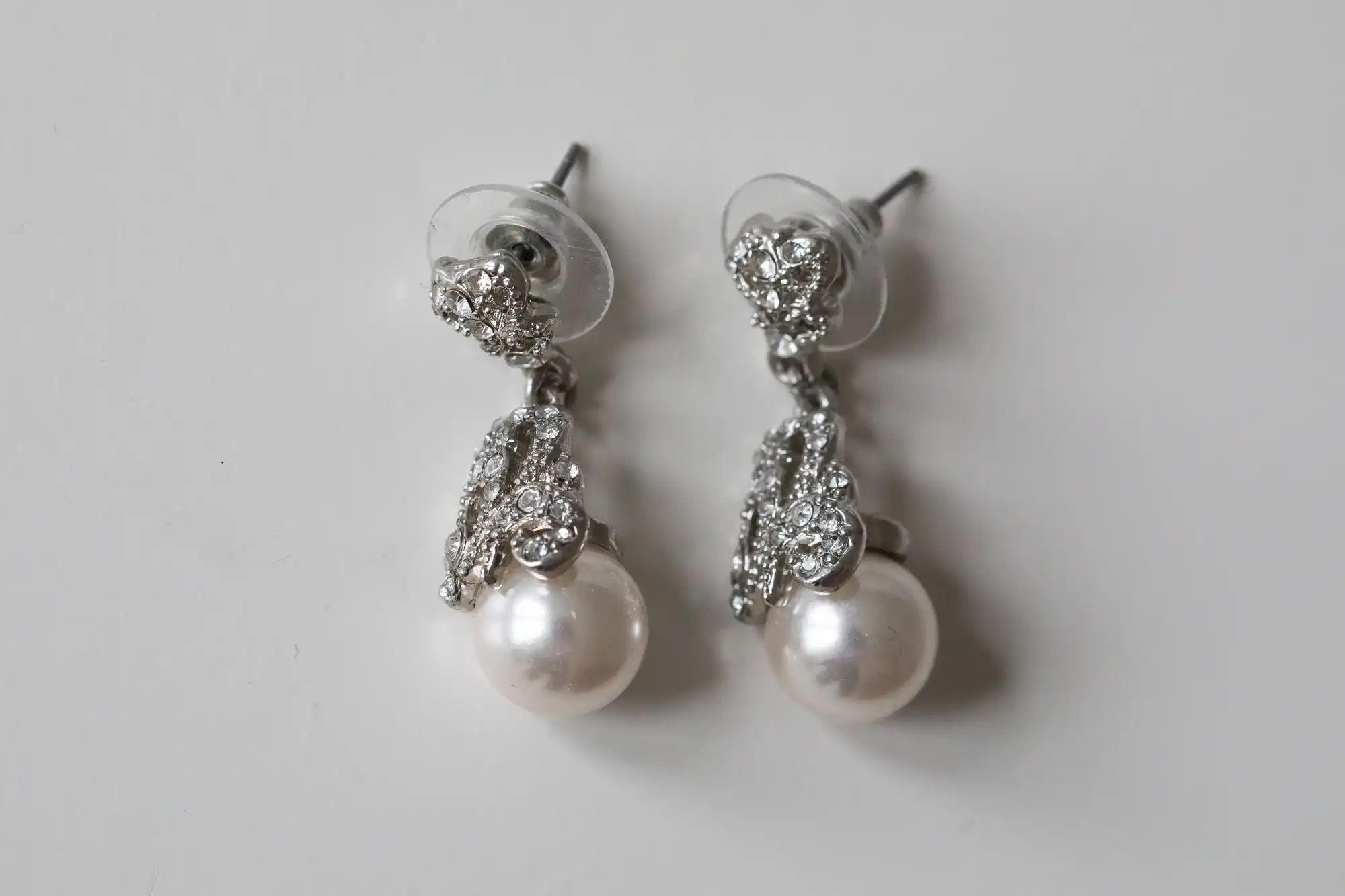 A pair of pearl and diamond drop earrings with silver studs on a plain white background.