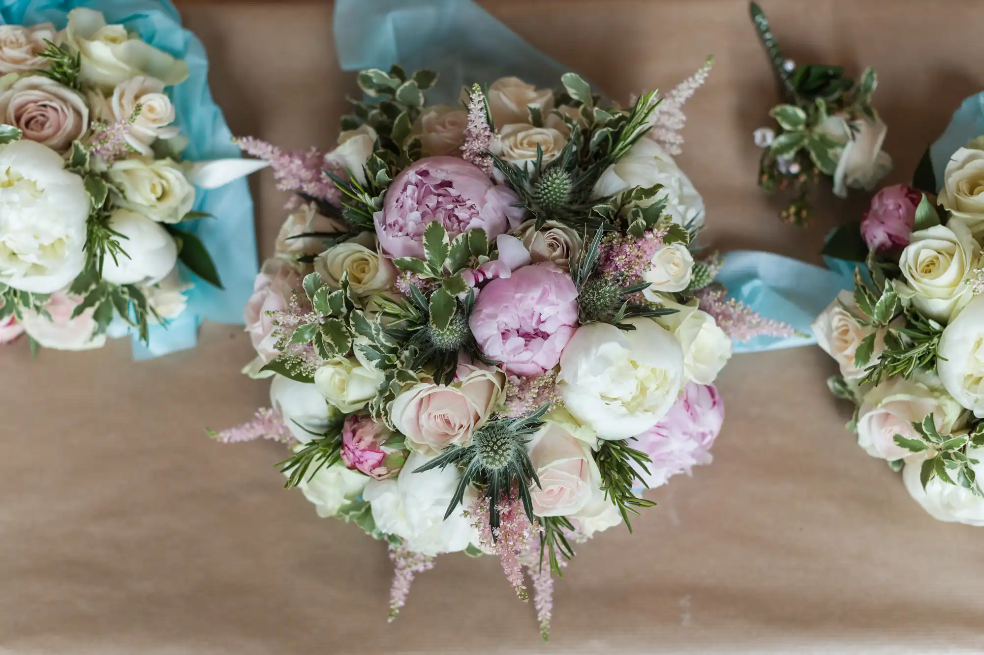 A floral arrangement featuring white and pink peonies, roses, and greenery, placed on a light brown surface with a blue ribbon.