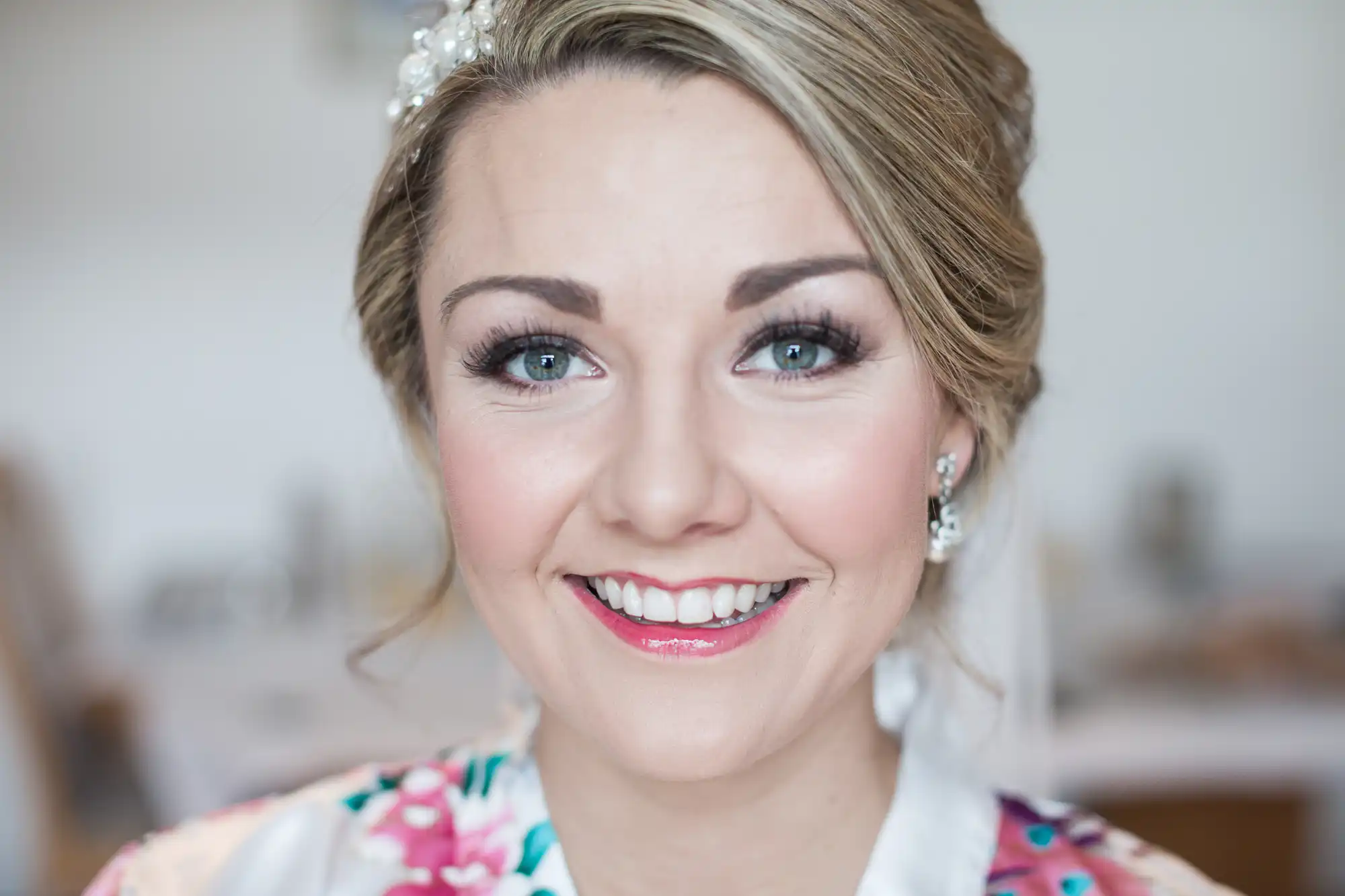 A woman with light makeup, a headpiece, and wearing floral attire smiles directly at the camera.