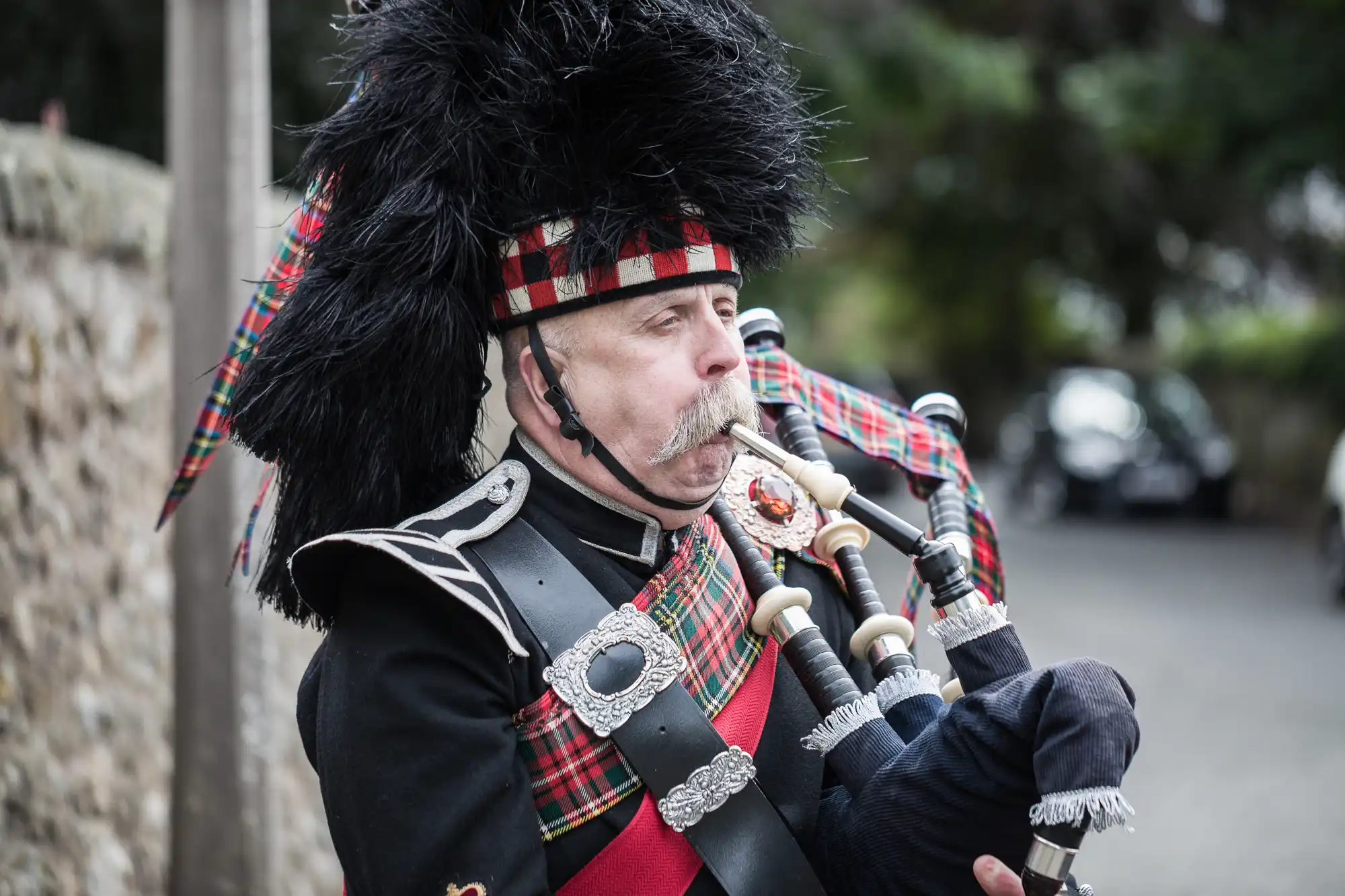 A man dressed in traditional Scottish attire plays the bagpipes outdoors.