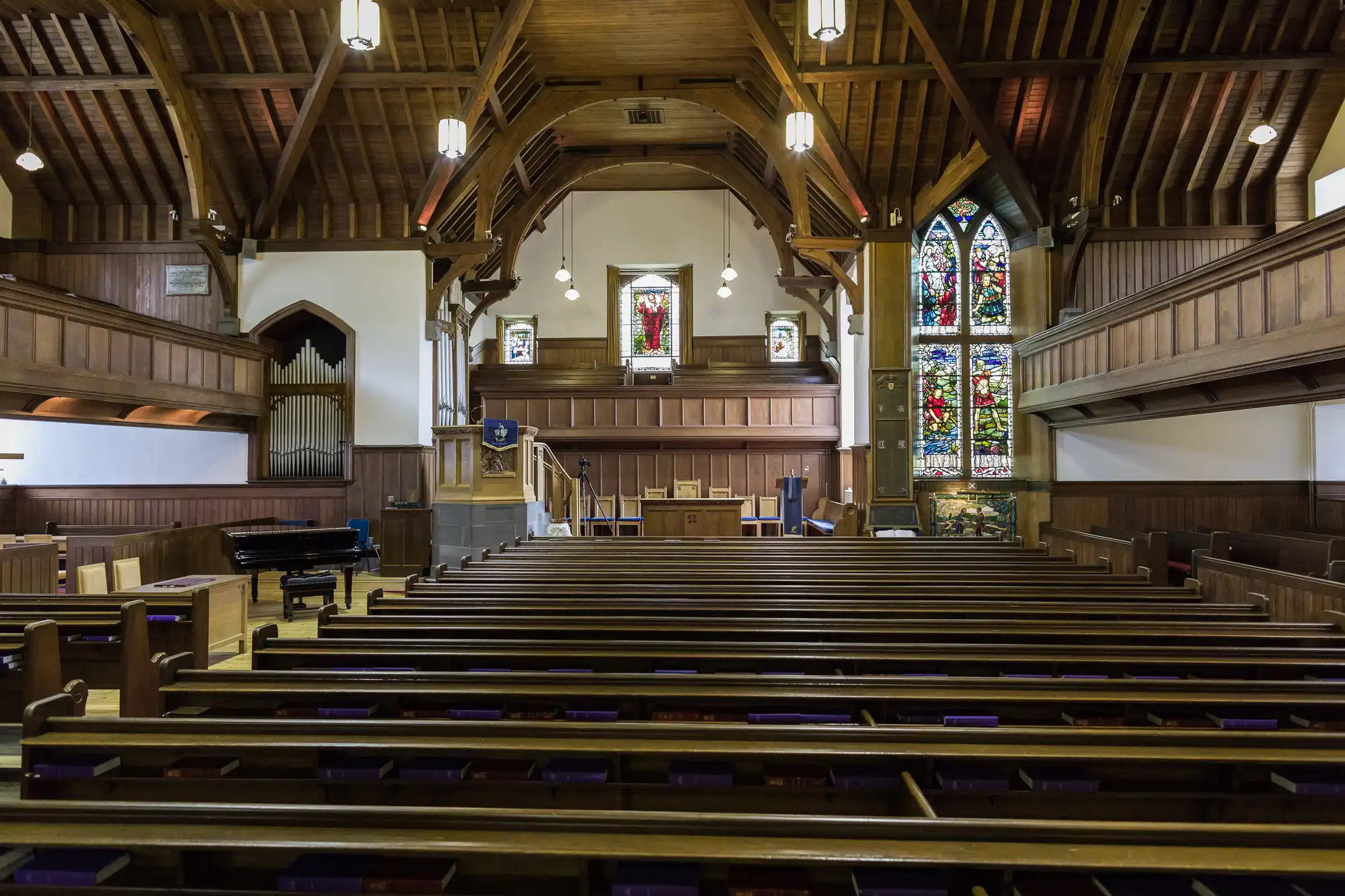 Interior view of an empty church with wooden pews, stained glass windows, and a raised altar area at the front.