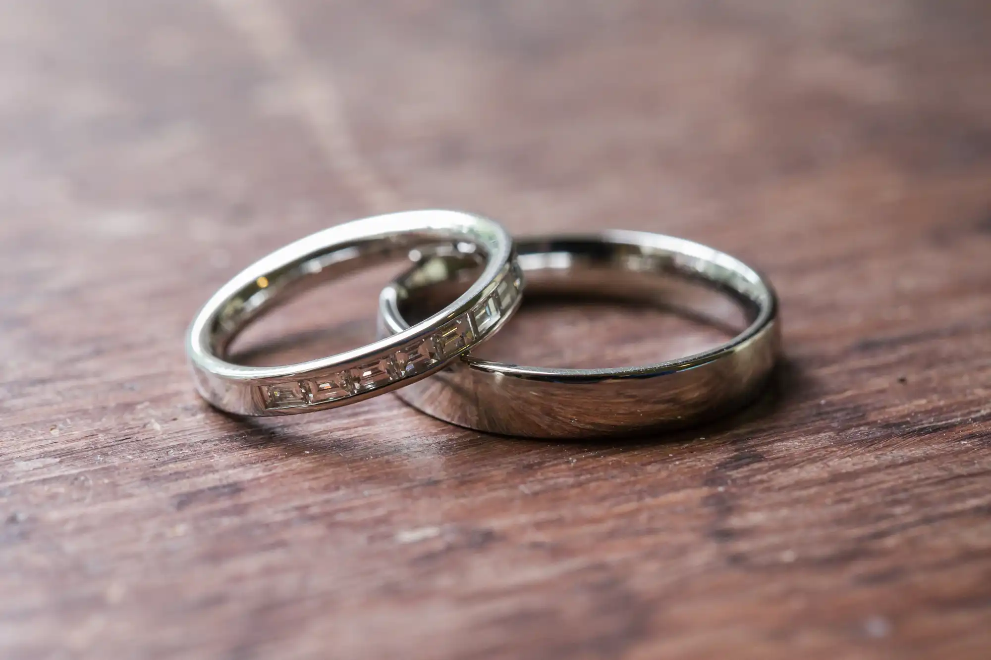 Two silver rings, one with rectangular engravings and the other plain, resting on a wooden surface.