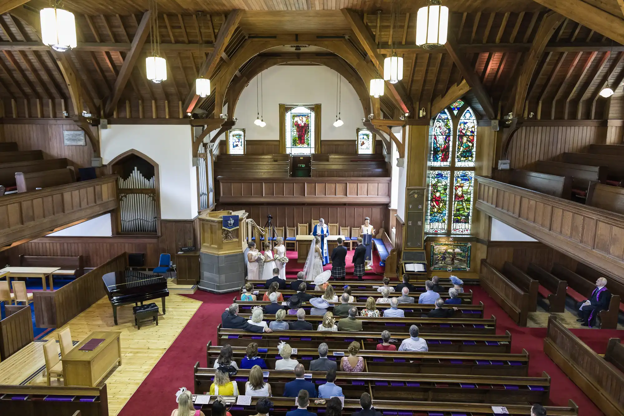 People attending a service in a church with wooden interiors, stained glass windows, and a high ceiling.