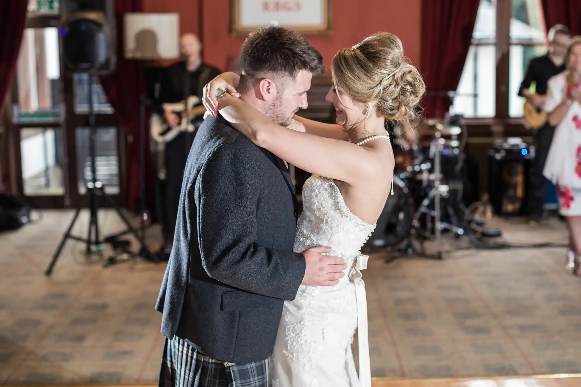 A couple in formal attire shares a dance at an indoor event, with a live band performing in the background.