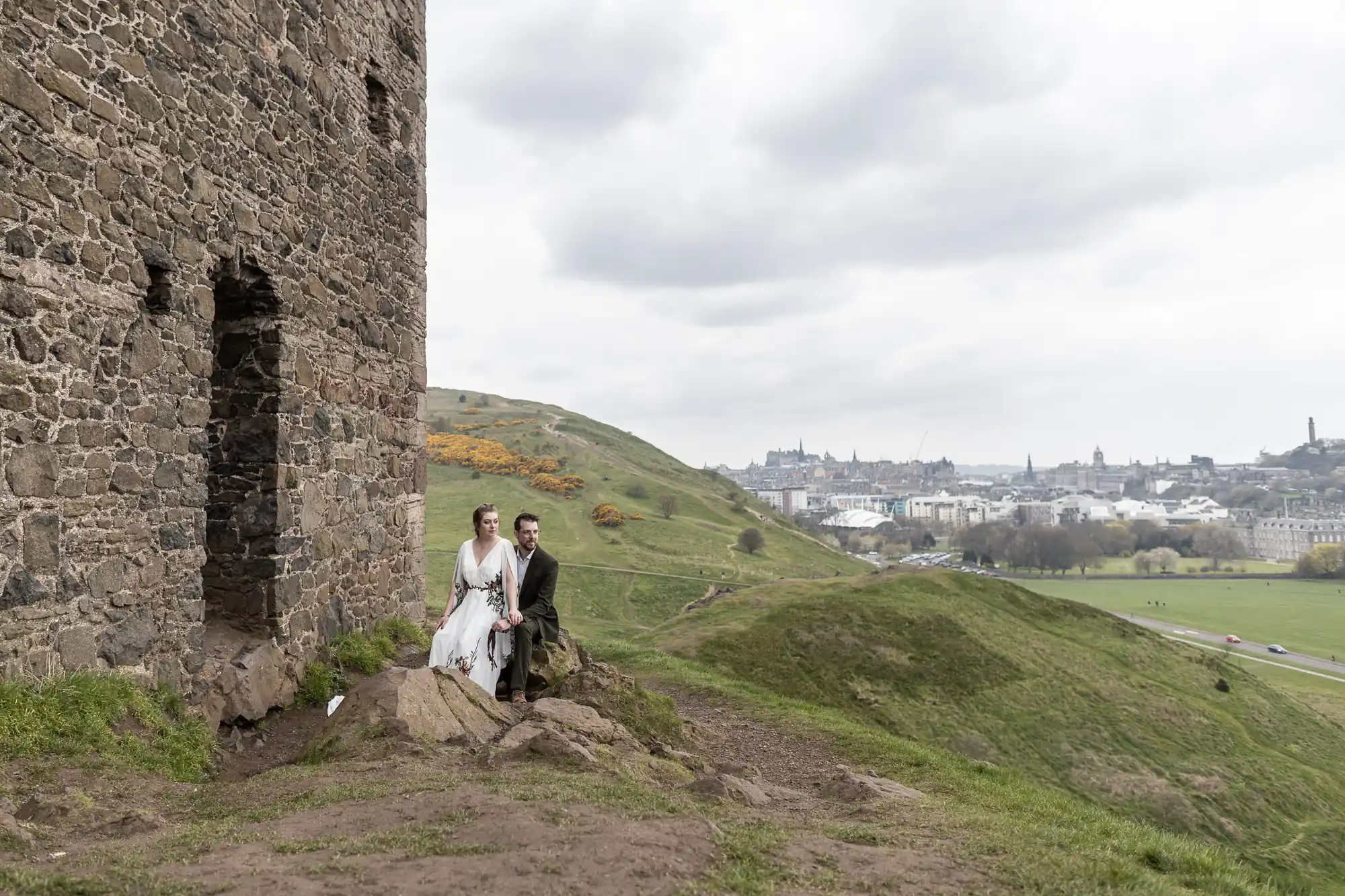 newlyweds sat beside ruin chapel with city backdrop