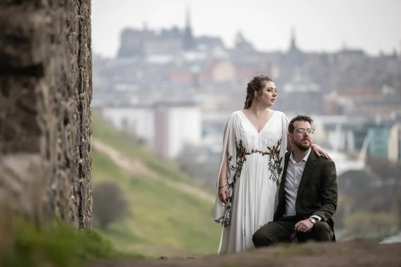 Scotland elopement newlyweds sat next to St Anthony's Chapel ruin with city centre in background