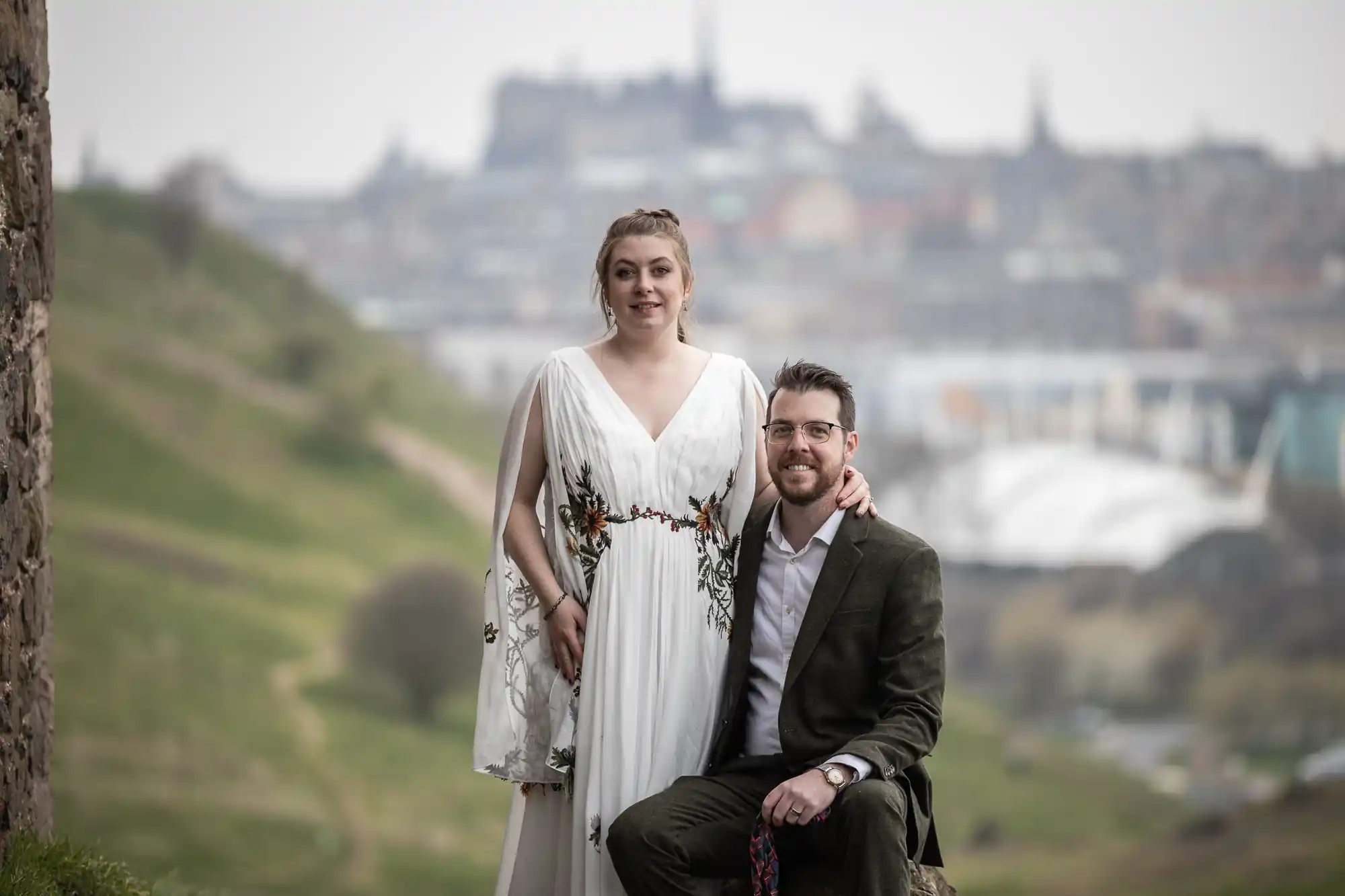 newlyweds beside ruin chapel with city backdrop