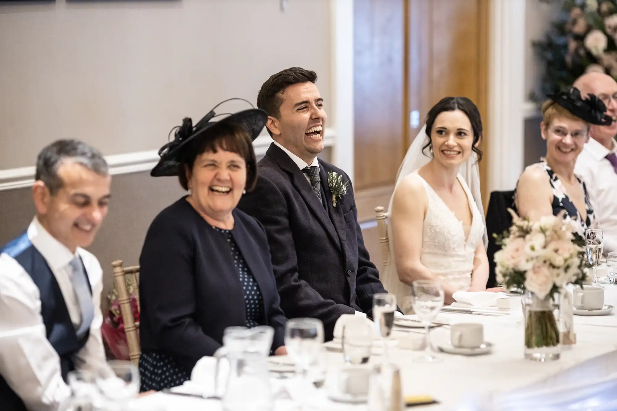 A group of people in formal attire seated at a table, smiling and laughing.