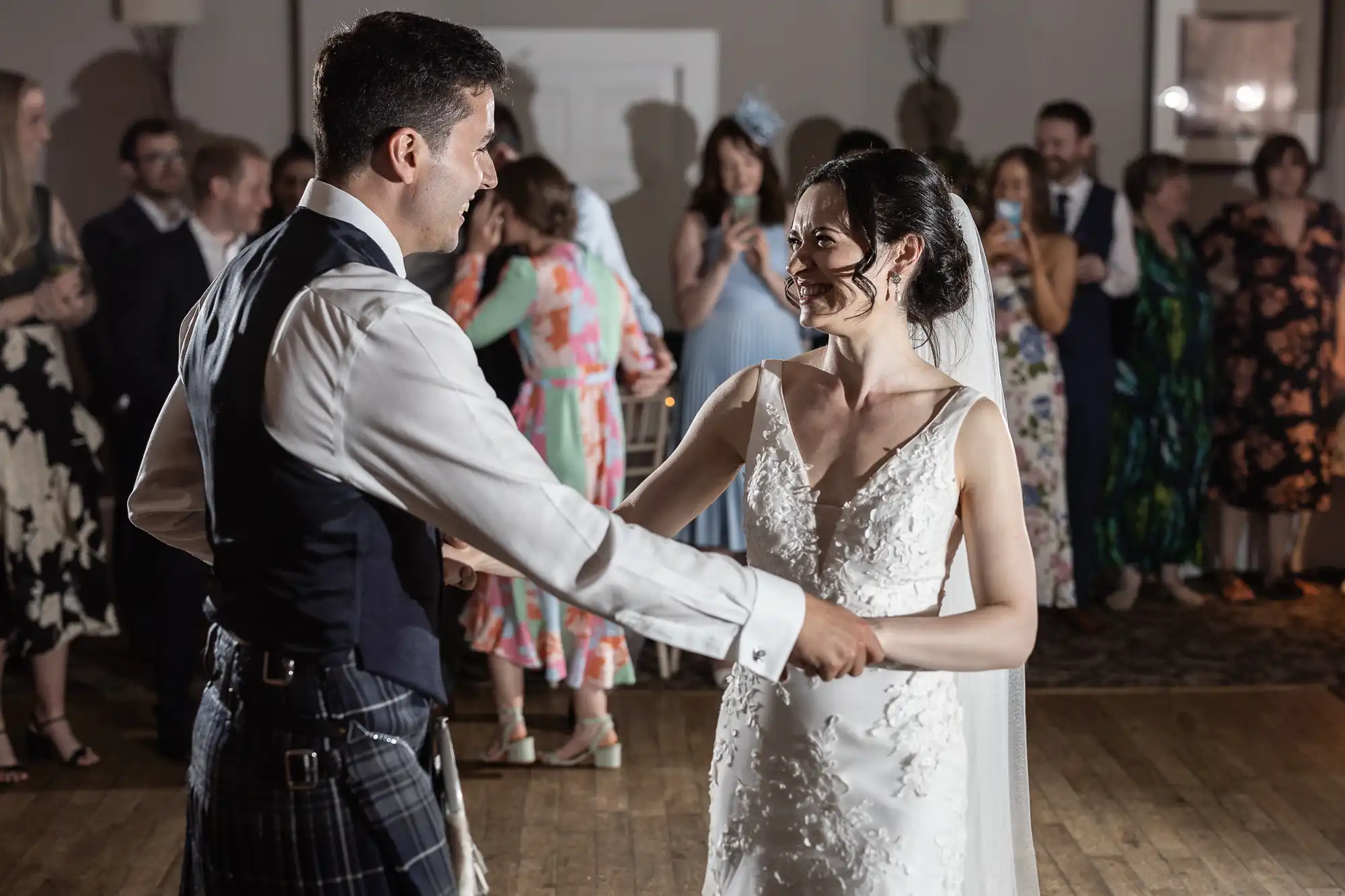 A bride and groom dance together at a wedding reception, with guests watching in the background.