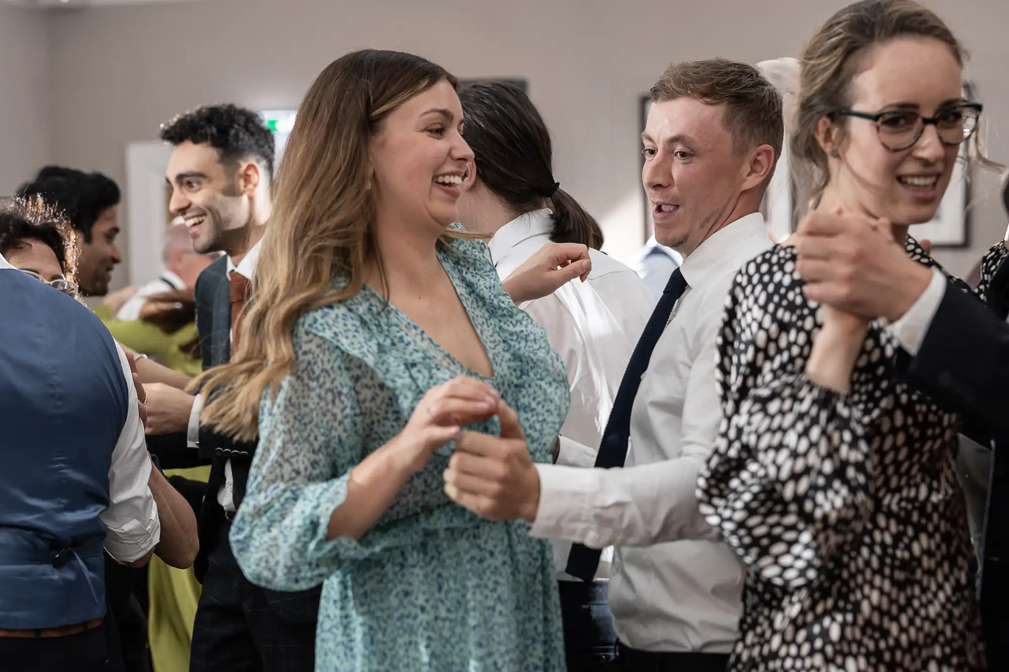 Group of people in semi-formal attire, smiling and dancing closely together in a social setting.