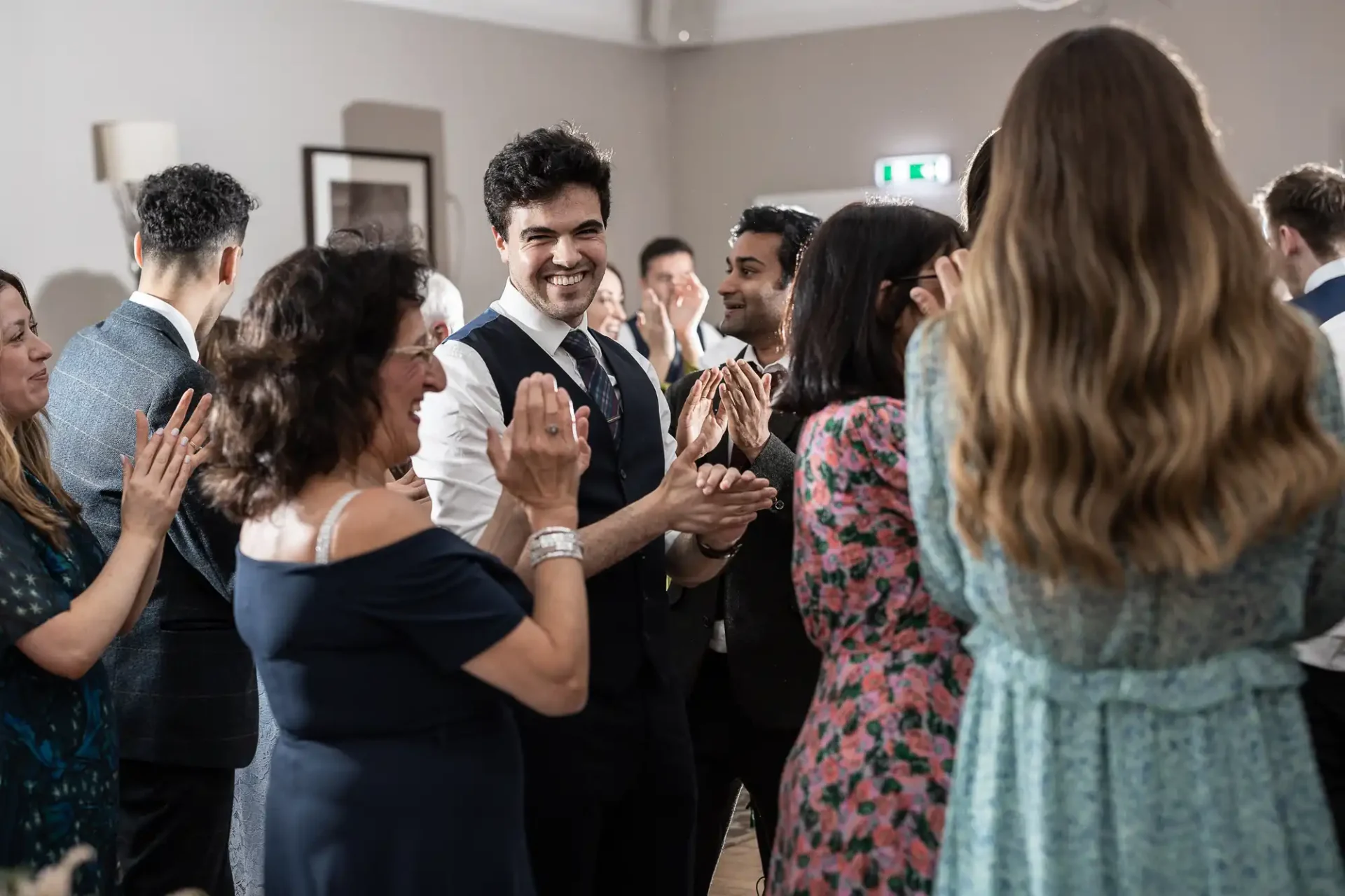 A group of people in formal attire clapping and smiling at an indoor event.