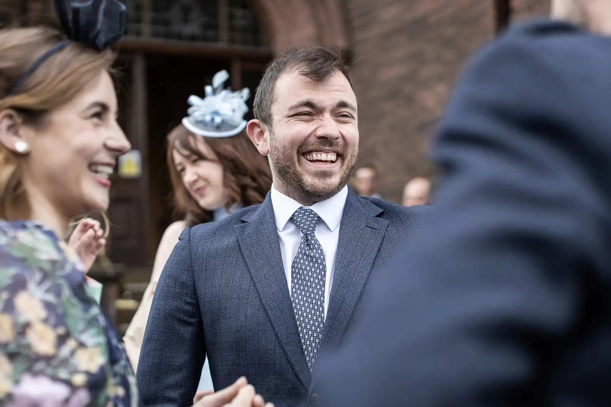 A man in a suit smiles while standing among people in formal attire.