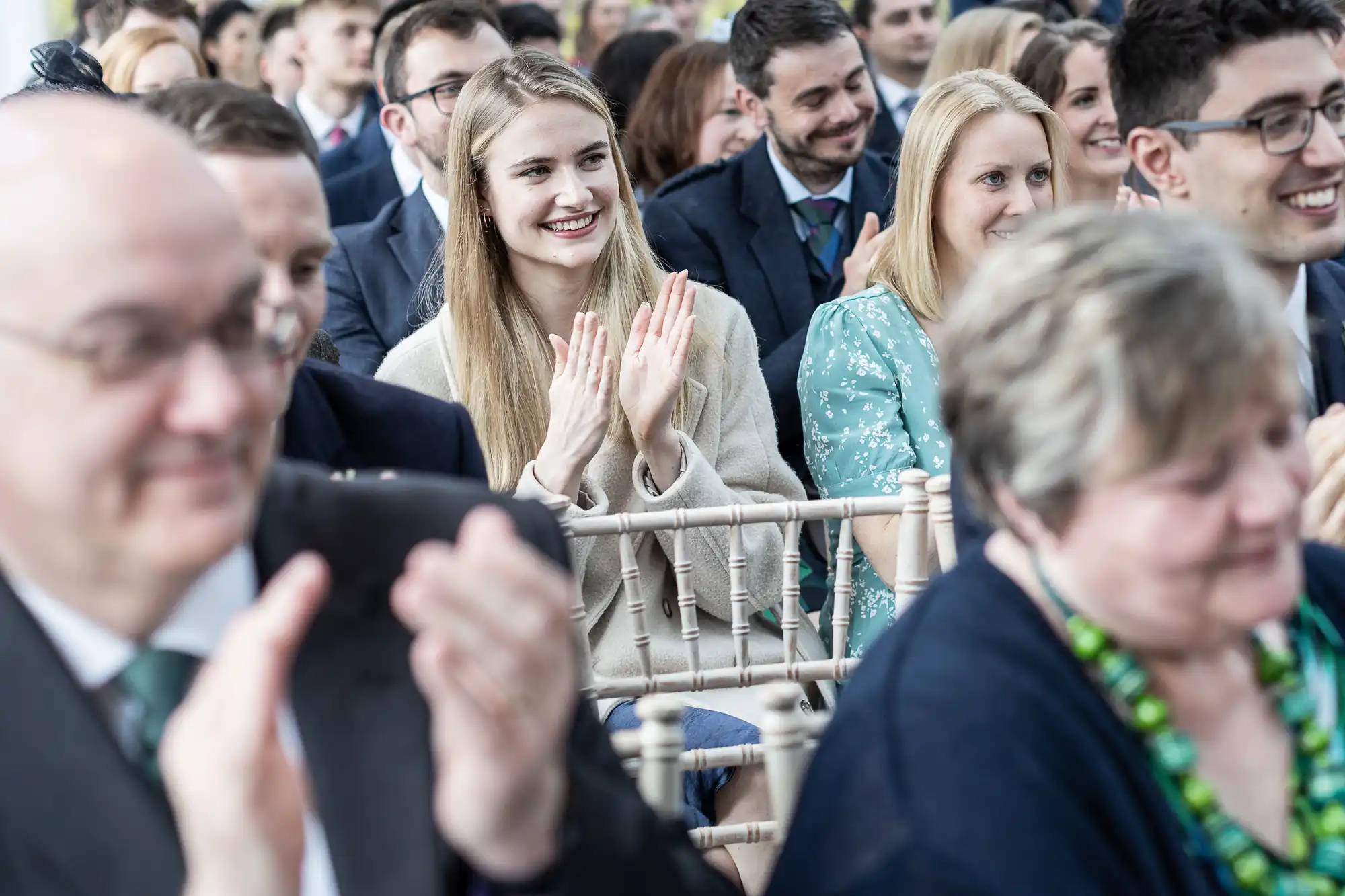 Audience members sitting and clapping during an event, with a focus on a young woman smiling in the center.