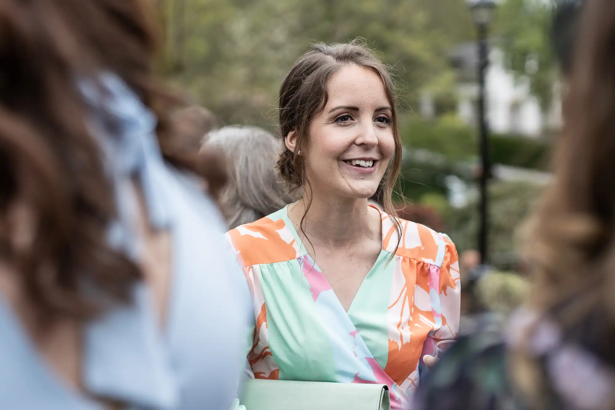 Woman smiling outdoors in a colorful dress, surrounded by people.