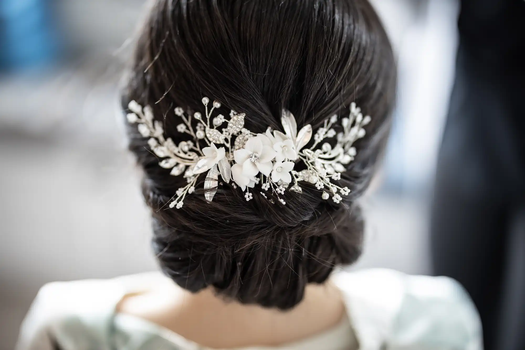 Close-up of an elegant updo hairstyle adorned with a decorative white floral hairpiece featuring small pearls and delicate silver branches.