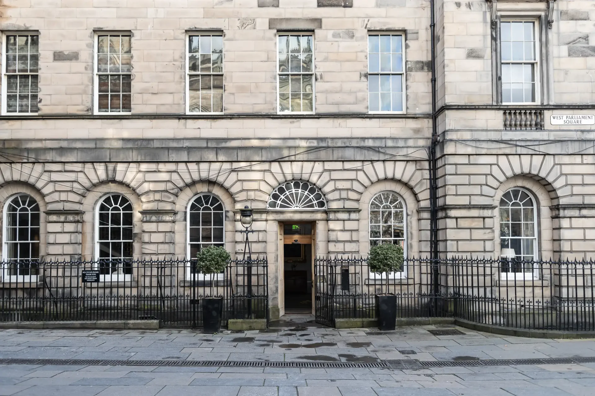 An elegant entrance to a stone building with arched doorways, metal security gates, and a sign reading "st. andrew square edinburgh".