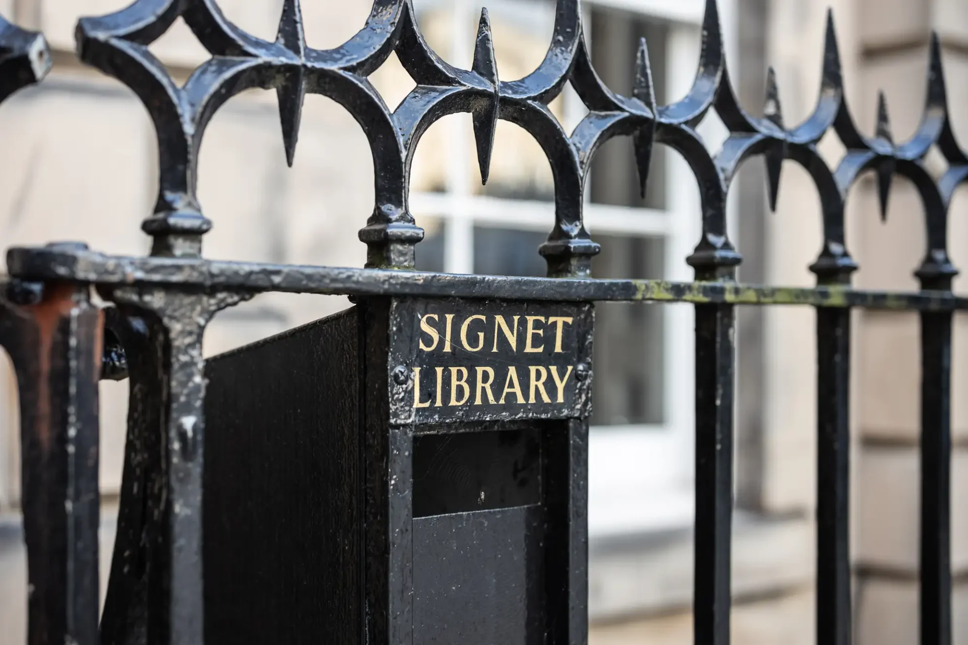 Close-up of a black iron fence with sharp, ornate spikes and a plate marked "signet library" attached to one of the bars.