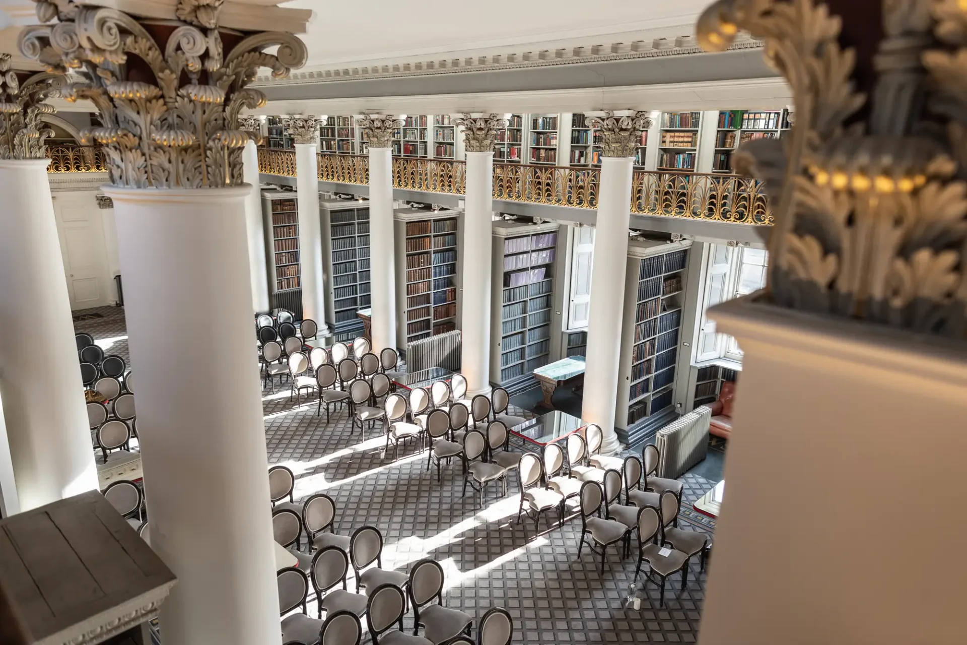 Elegant library hall with rows of empty chairs, surrounded by tall columns and ornate balconies filled with books.