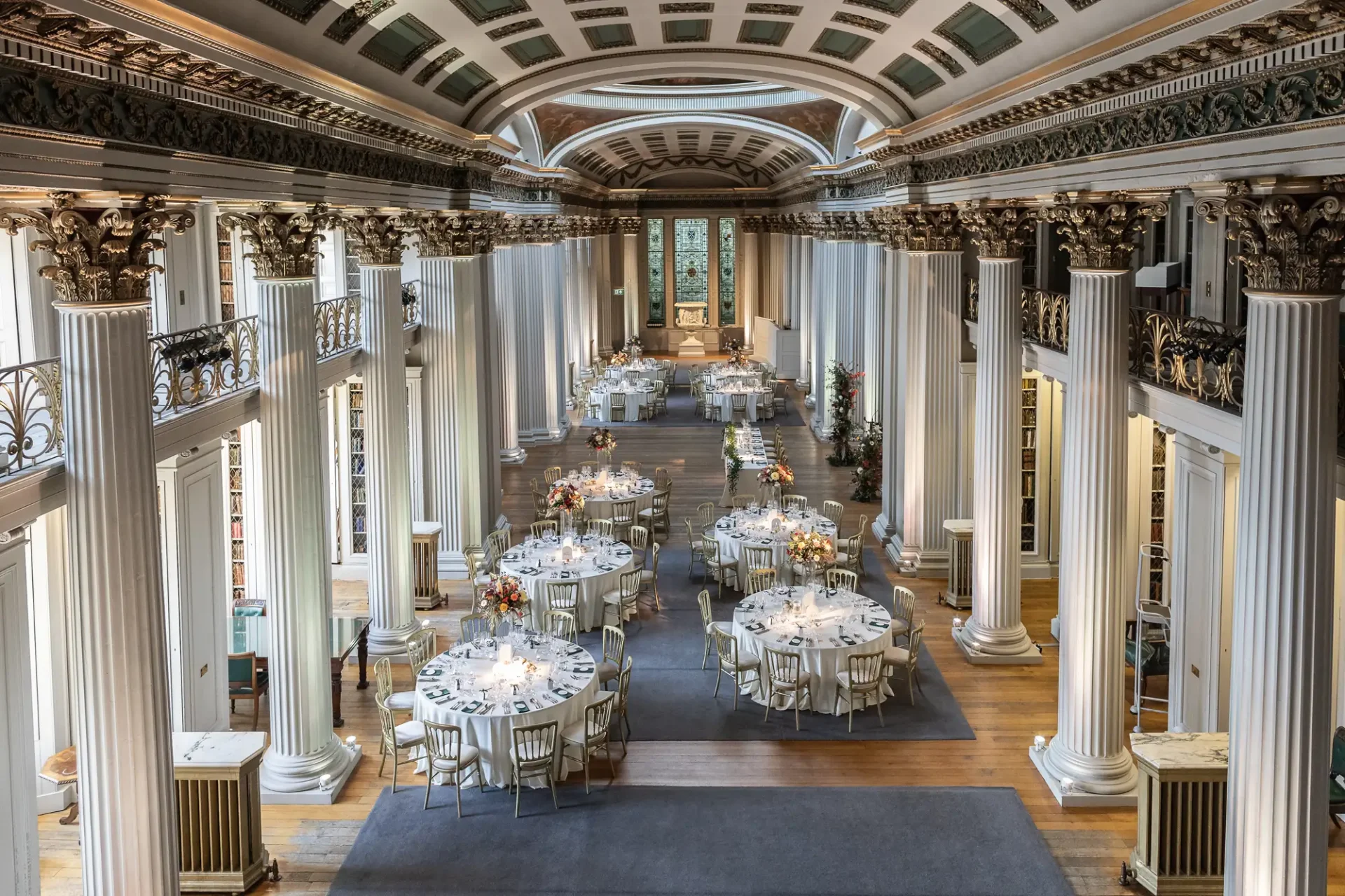 Elegant dining hall with round tables set for an event, featuring classical white columns and ornate balconies.