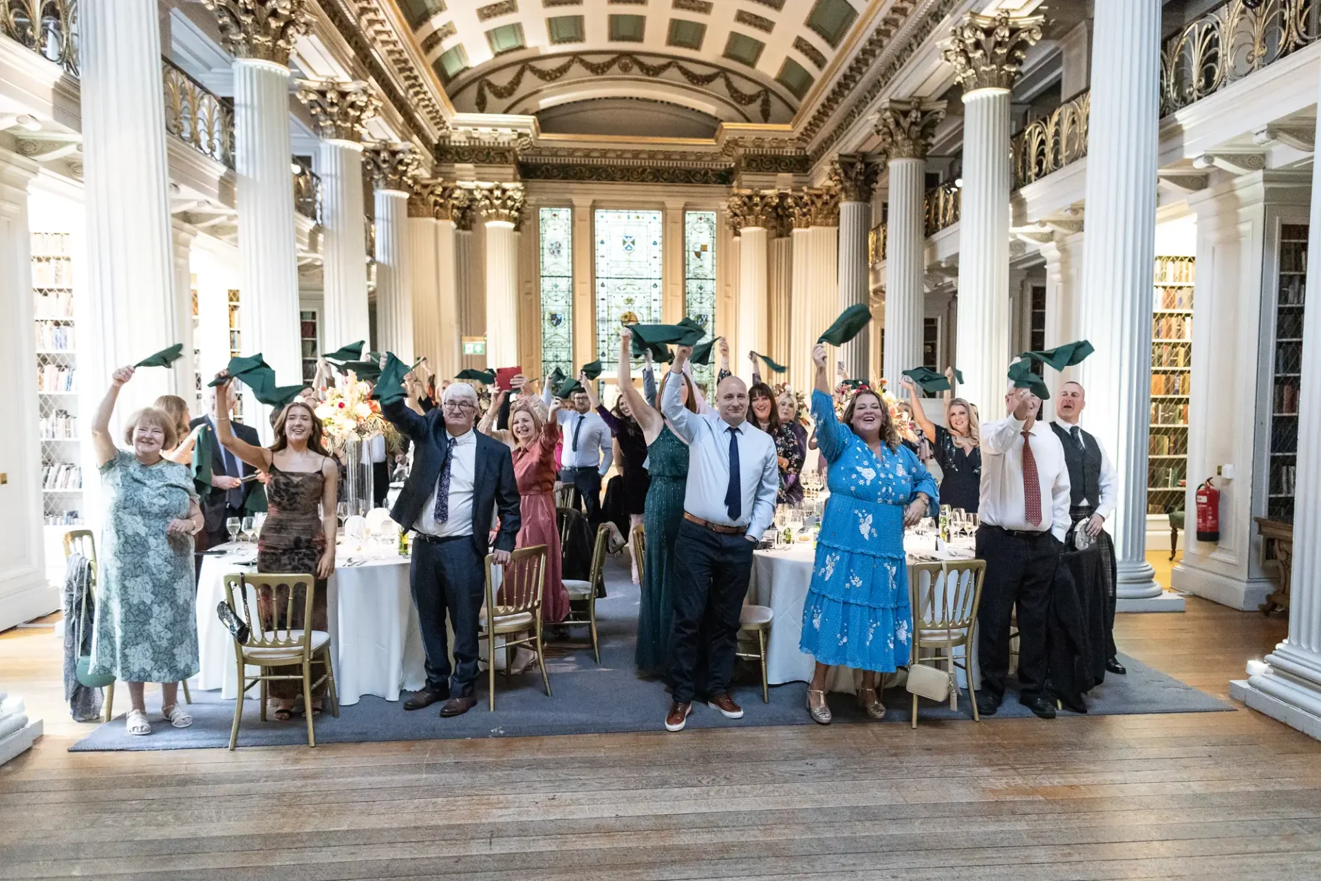 People joyfully tossing their graduation caps in the air at a formal dinner event in an elegant hall with classical architecture.