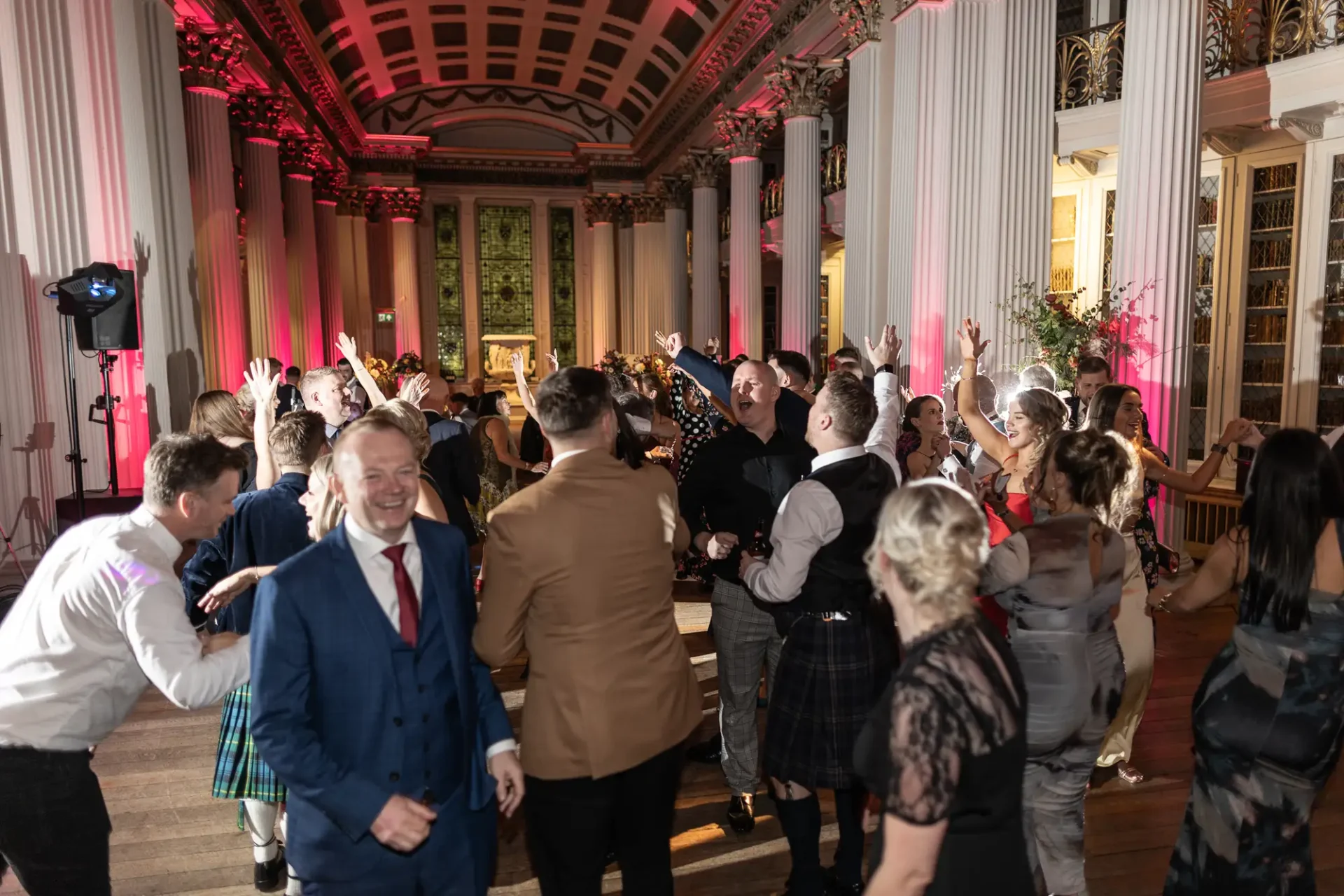 Guests in formal attire dancing and enjoying a celebration in an elegantly lit hall with classical architectural details.