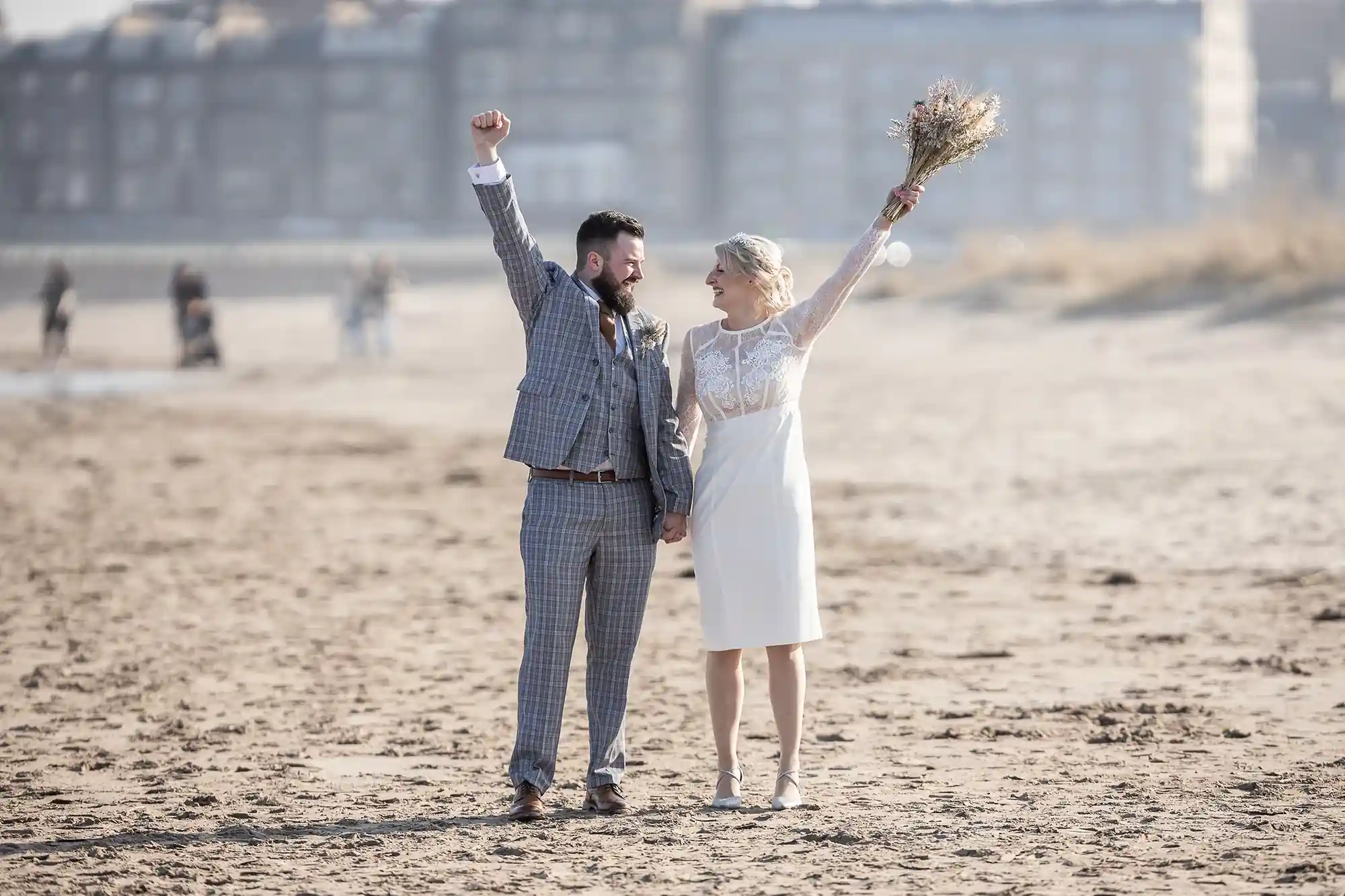 A joyful couple celebrates on a beach, with the woman holding a bouquet aloft and the man fist-pumping the air.