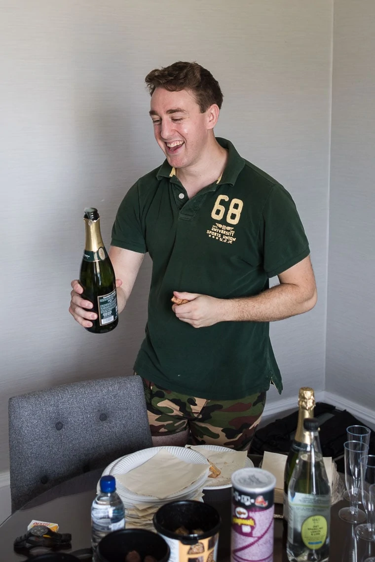 groom smiling opening a bottle of champagne