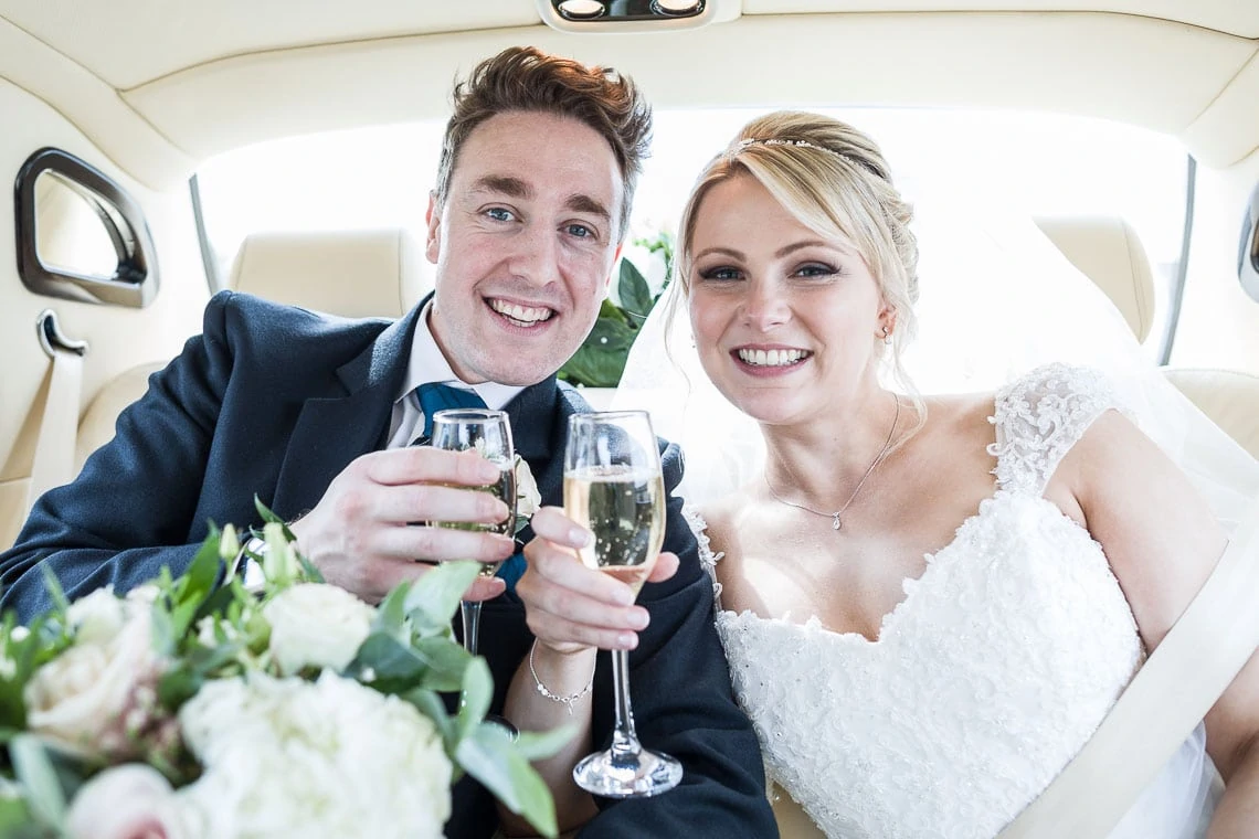 newlyweds toast with a glass of champagne in the back of a Bentley wedding car