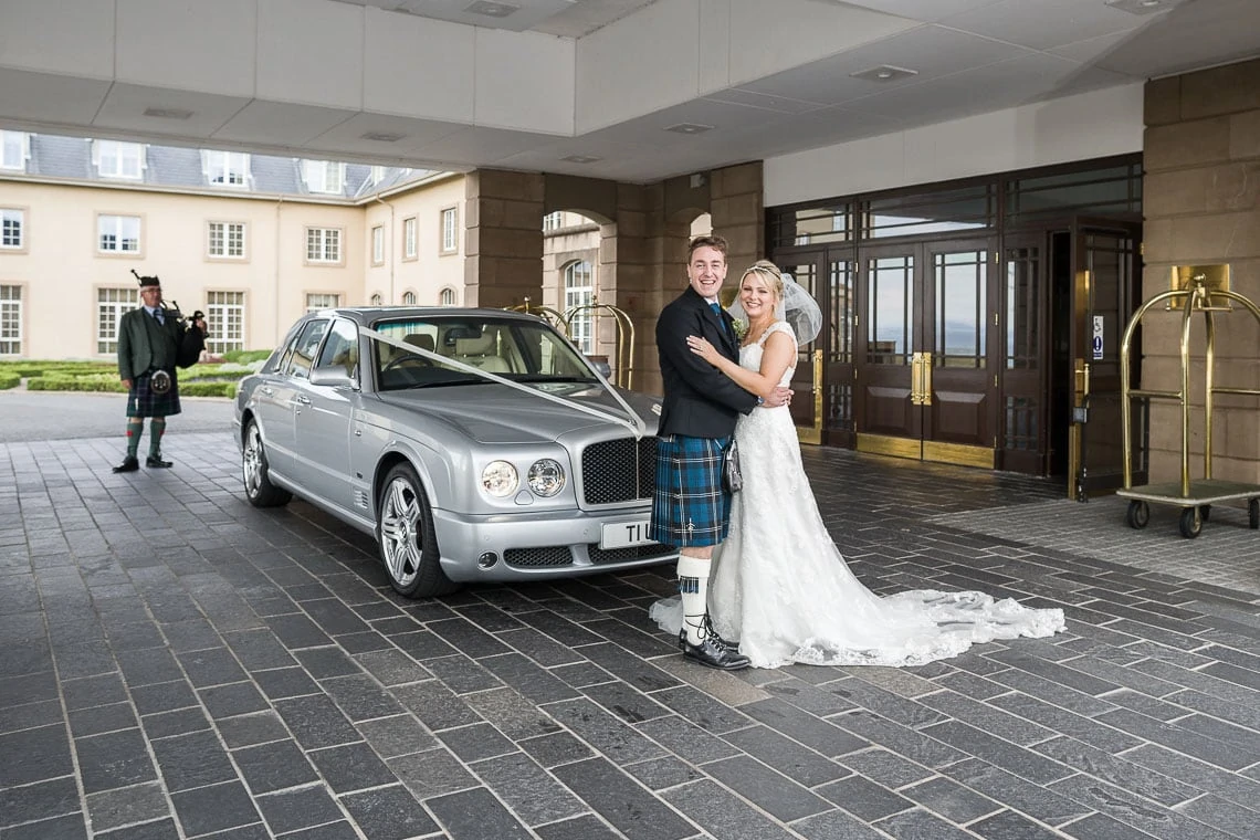 newlyweds standing in front of their Bentley wedding car at Fairmont St Andrews