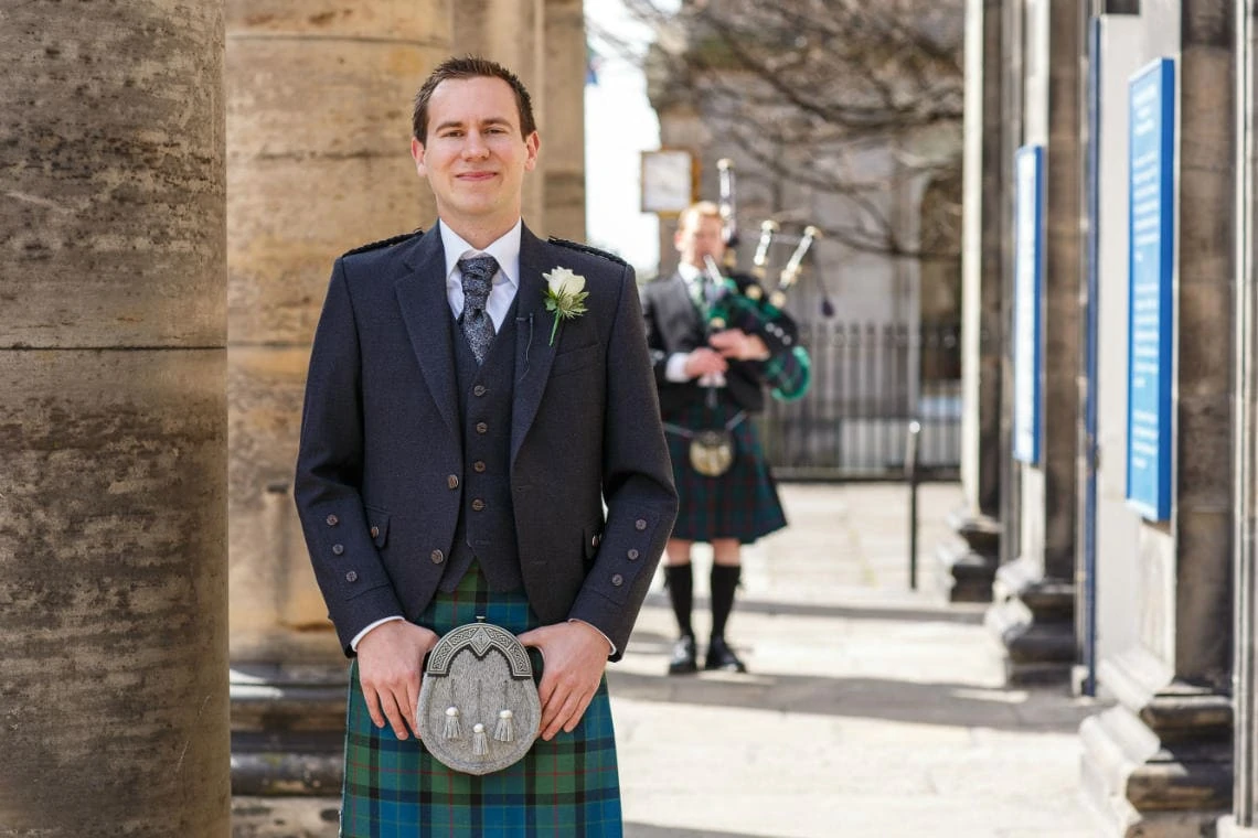 groom standing outside St Andrew's and St George's West Church of Scotland with a piper in the background