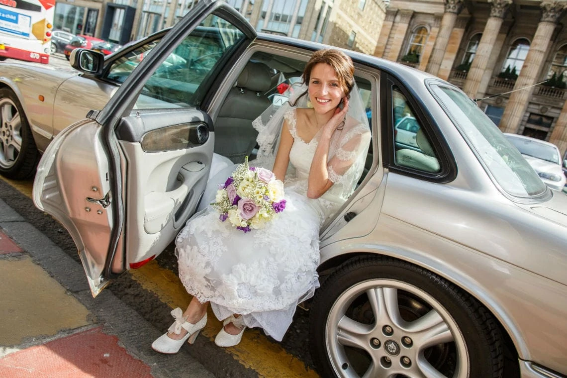 bride in white dress getting out of a Jaguar wedding car on George Street