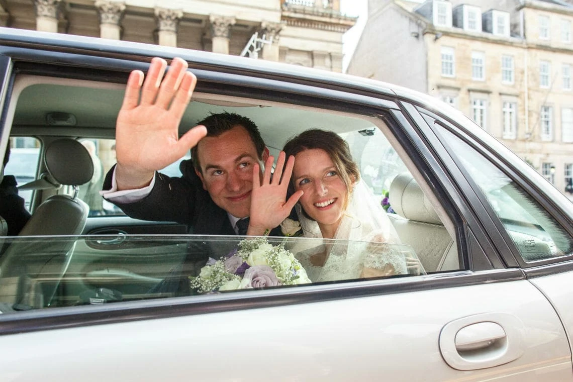 newlyweds waving out the window of their wedding car on George Street