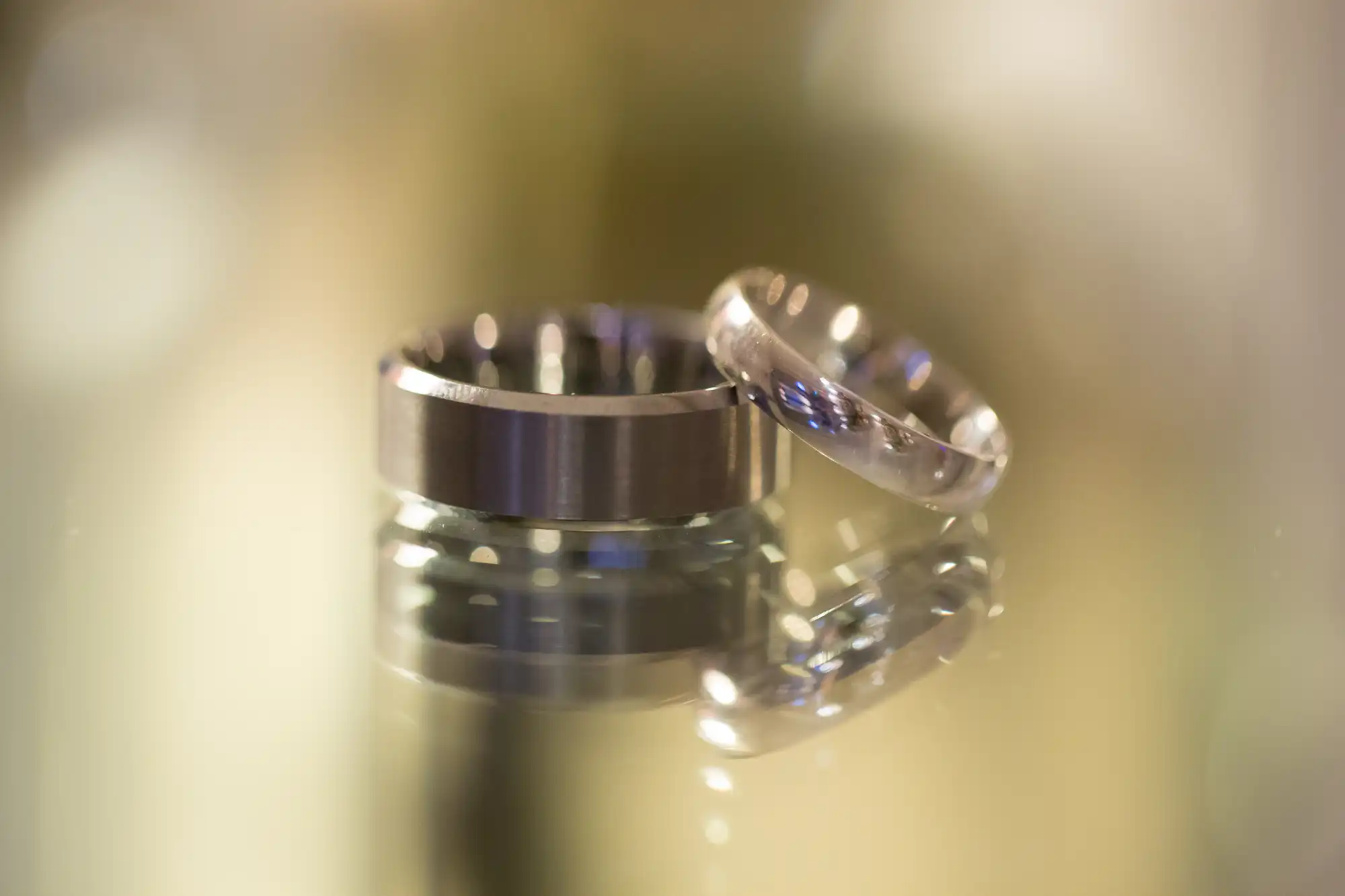 Two wedding rings focused in the foreground with a soft, blurred golden background.