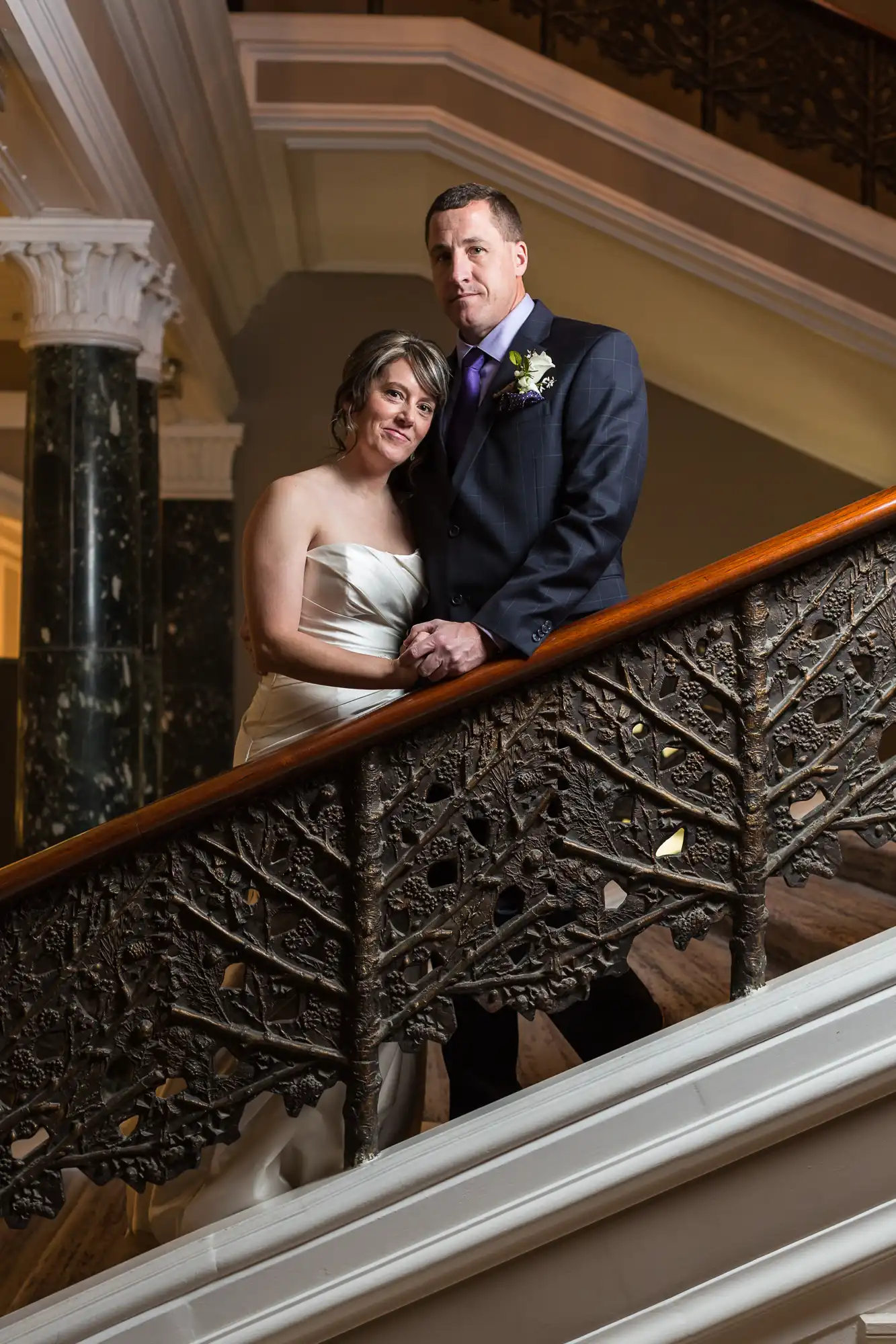 A bride and groom posing together on an ornate staircase.