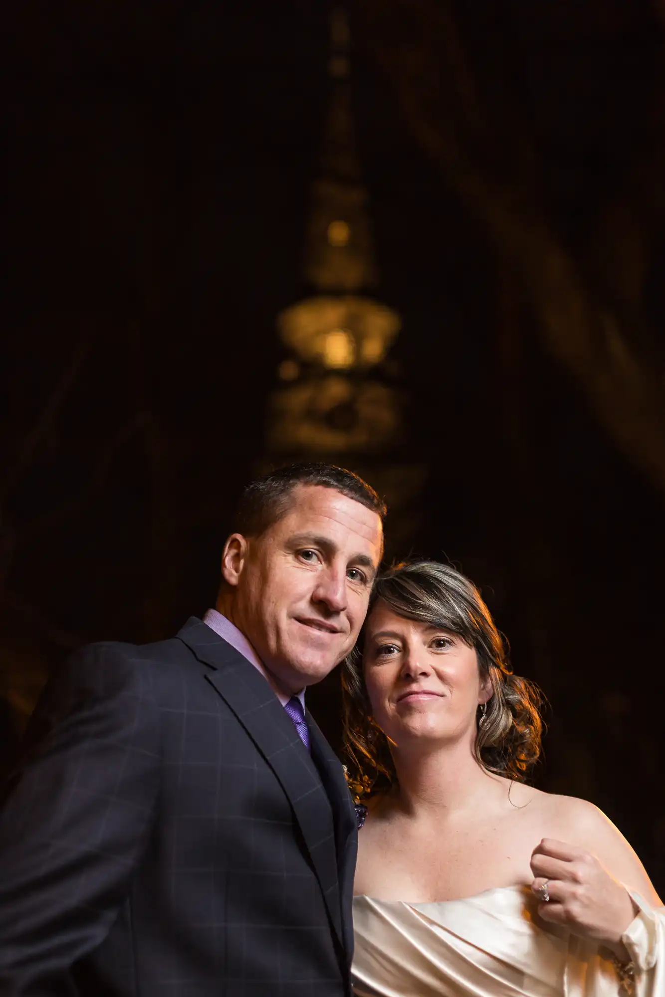 A couple posing for a portrait at night, with a softly lit, ornate spire in the background.