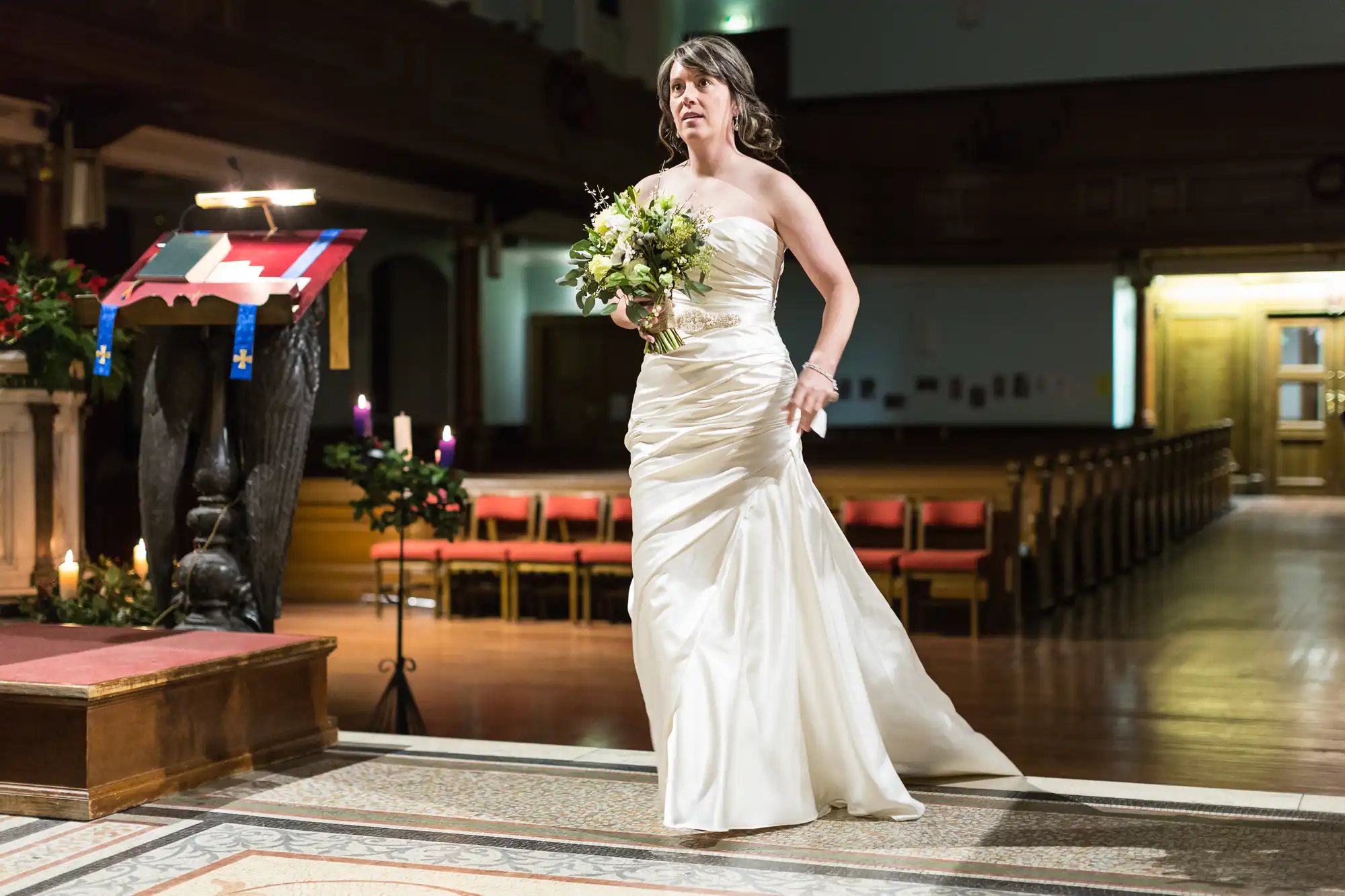 A bride in a strapless white gown holds a bouquet, looking anxious in a church aisle, with a casket draped in a national flag nearby.