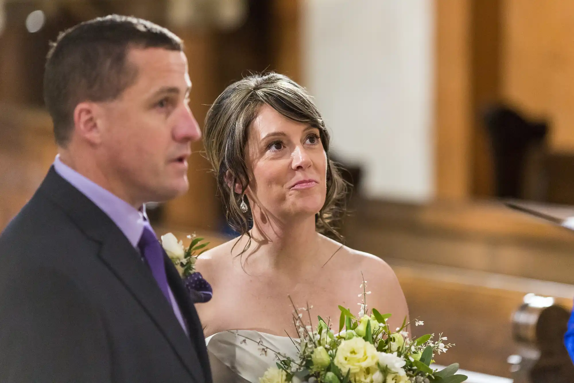 Bride and groom attentively listening during wedding ceremony in a church, bride holding a bouquet of white flowers.