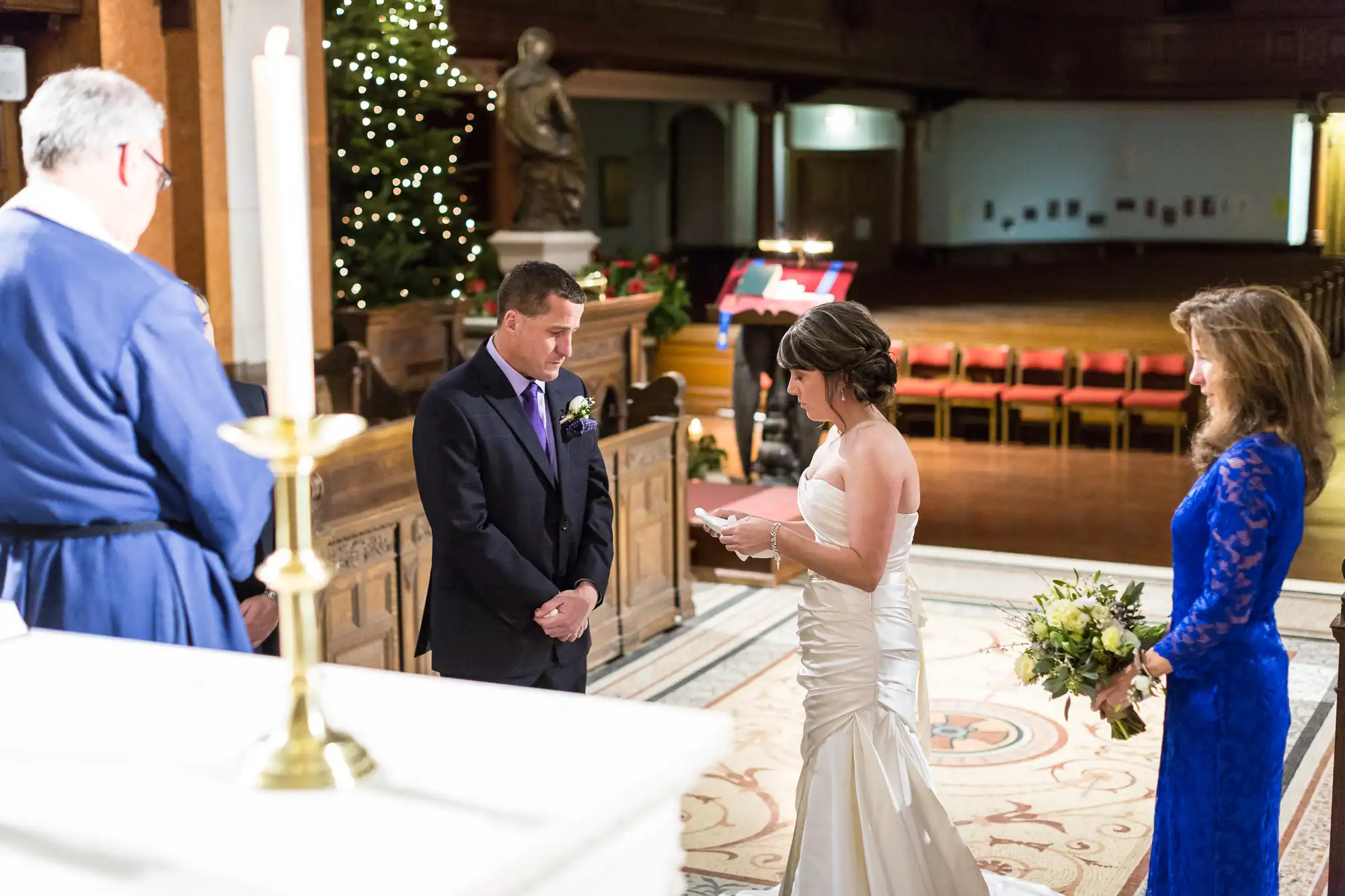 A bride and groom exchanging vows in a church, with an officiant and another woman present, during a wedding ceremony.