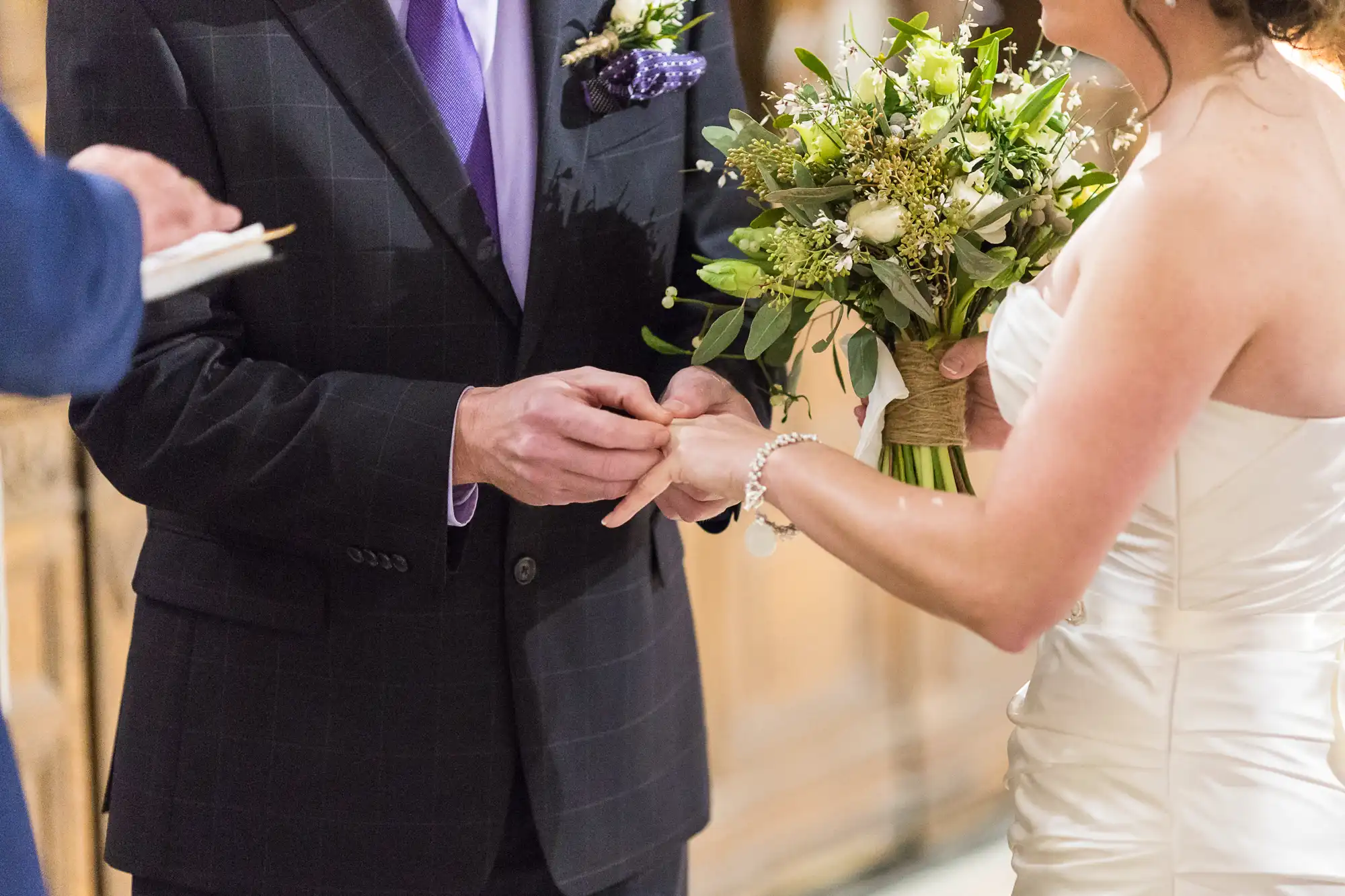 A bride and groom exchanging rings during a wedding ceremony, with the bride holding a bouquet of white and green flowers.