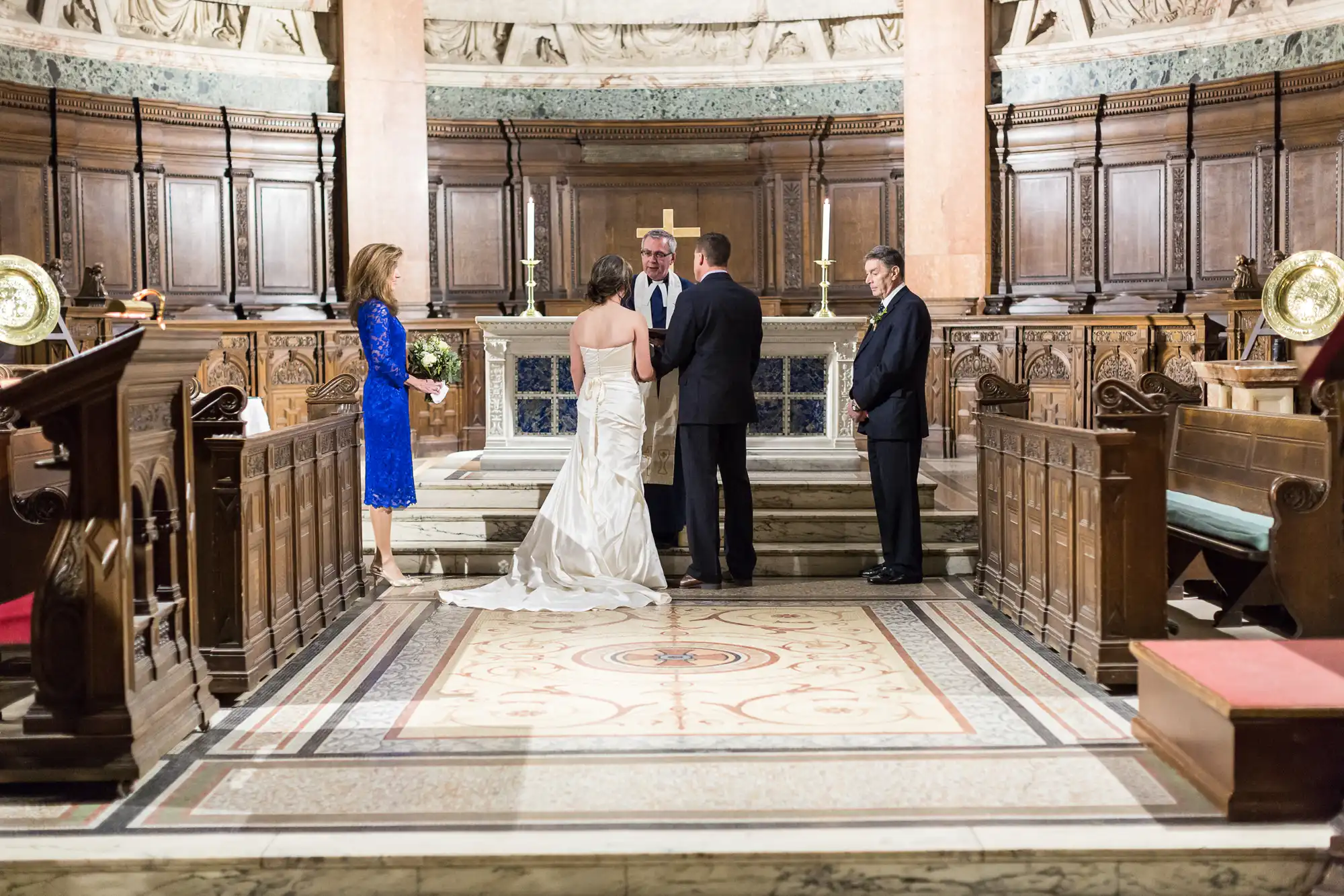 A wedding ceremony inside a grand church, featuring a bride in a white gown and a groom in a suit, standing before an officiant, with two witnesses nearby.