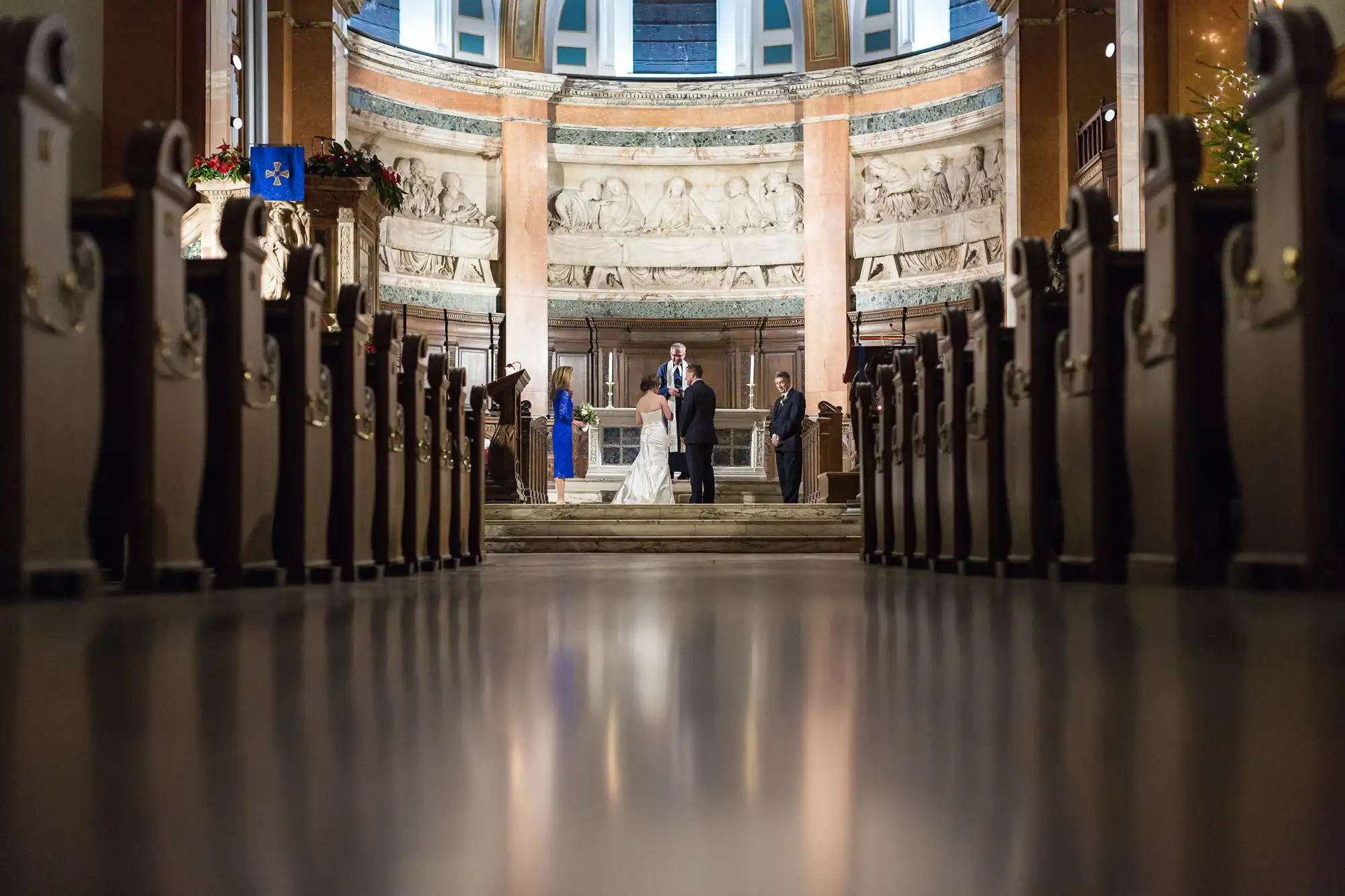 Wedding ceremony in a church, viewed between rows of pews, focusing on a couple at the altar with a few guests and eu flag visible.