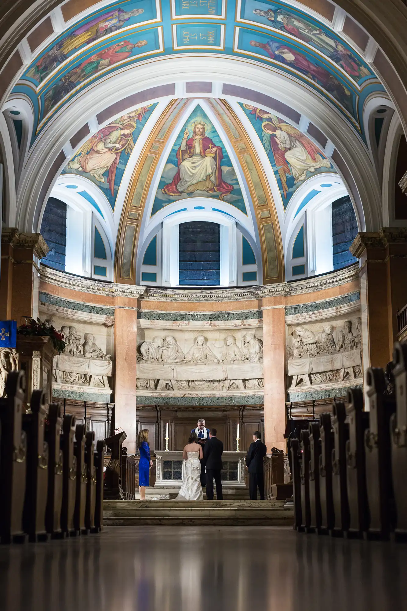 A bride and groom stand at the altar in a grand church with vibrant frescoes, flanked by marble columns, with guests in pews.
