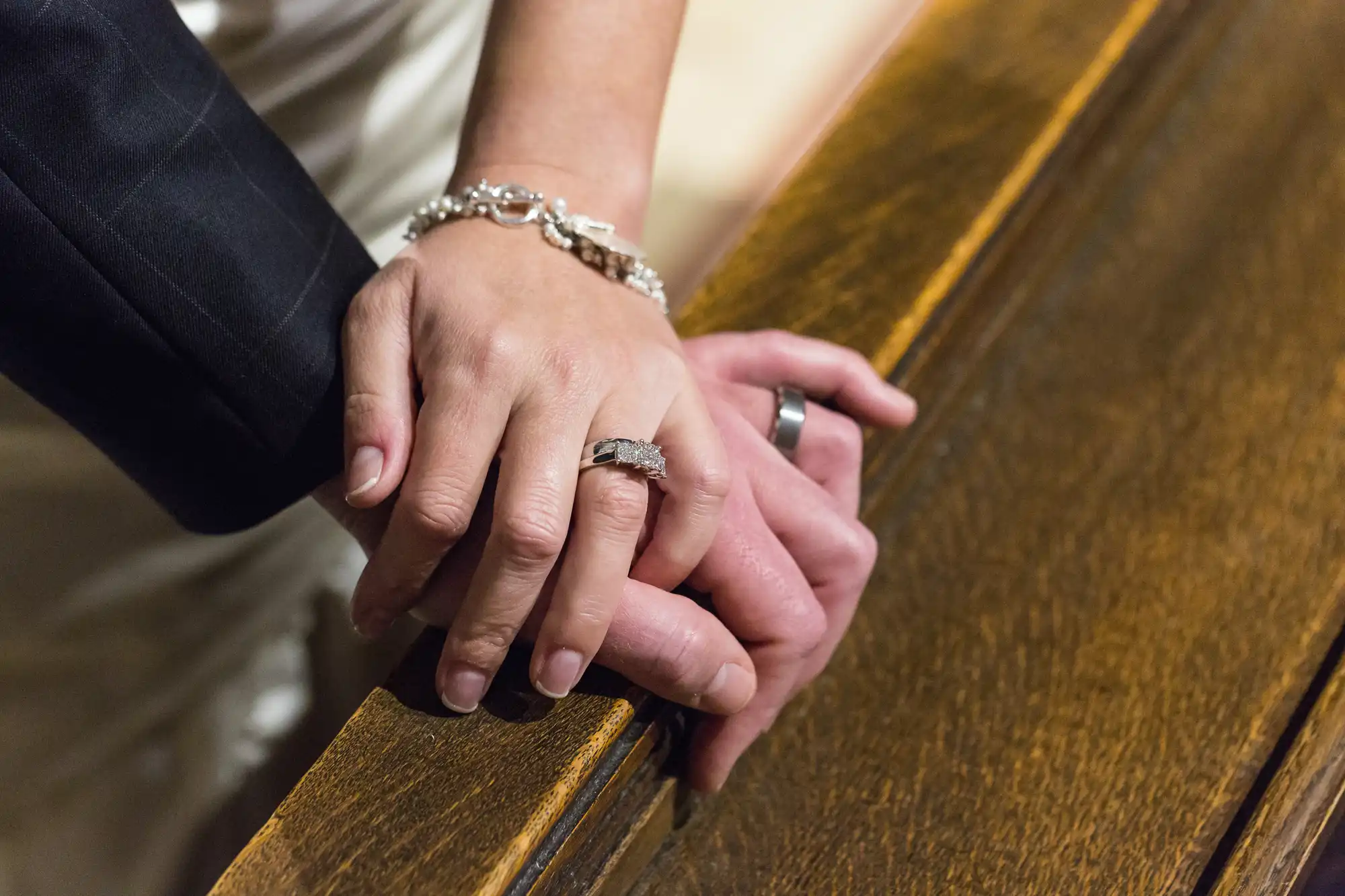Close-up of a married couple's hands resting on a wooden surface, showcasing their wedding rings.