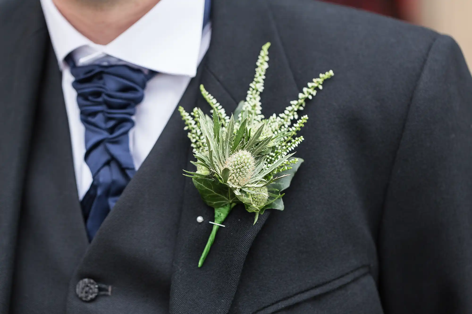 Close-up of a man in a suit with a blue ruffled tie, wearing a green and white floral boutonniere on his lapel.
