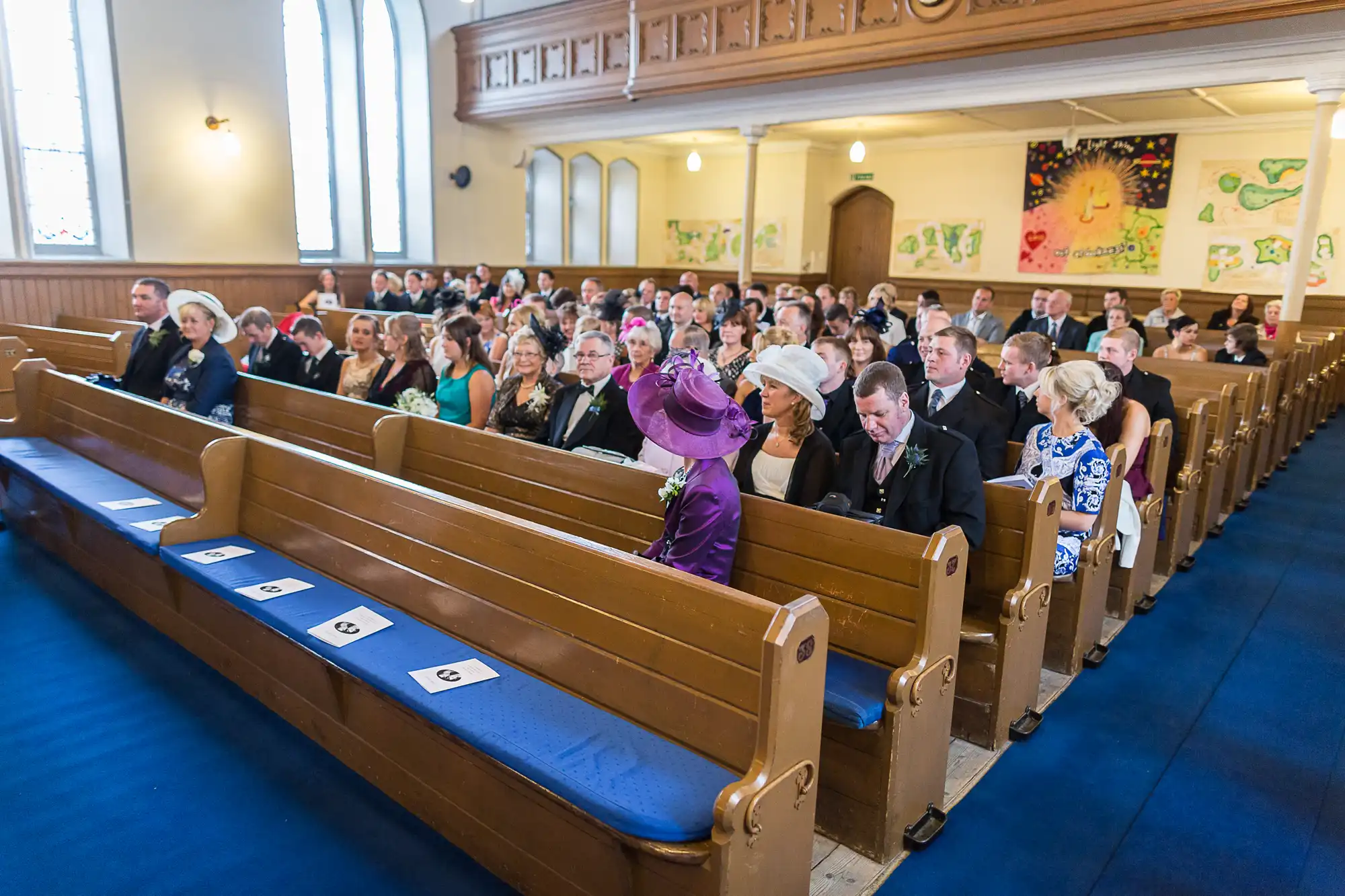 Guests seated in church pews during a wedding ceremony, dressed in formal attire.